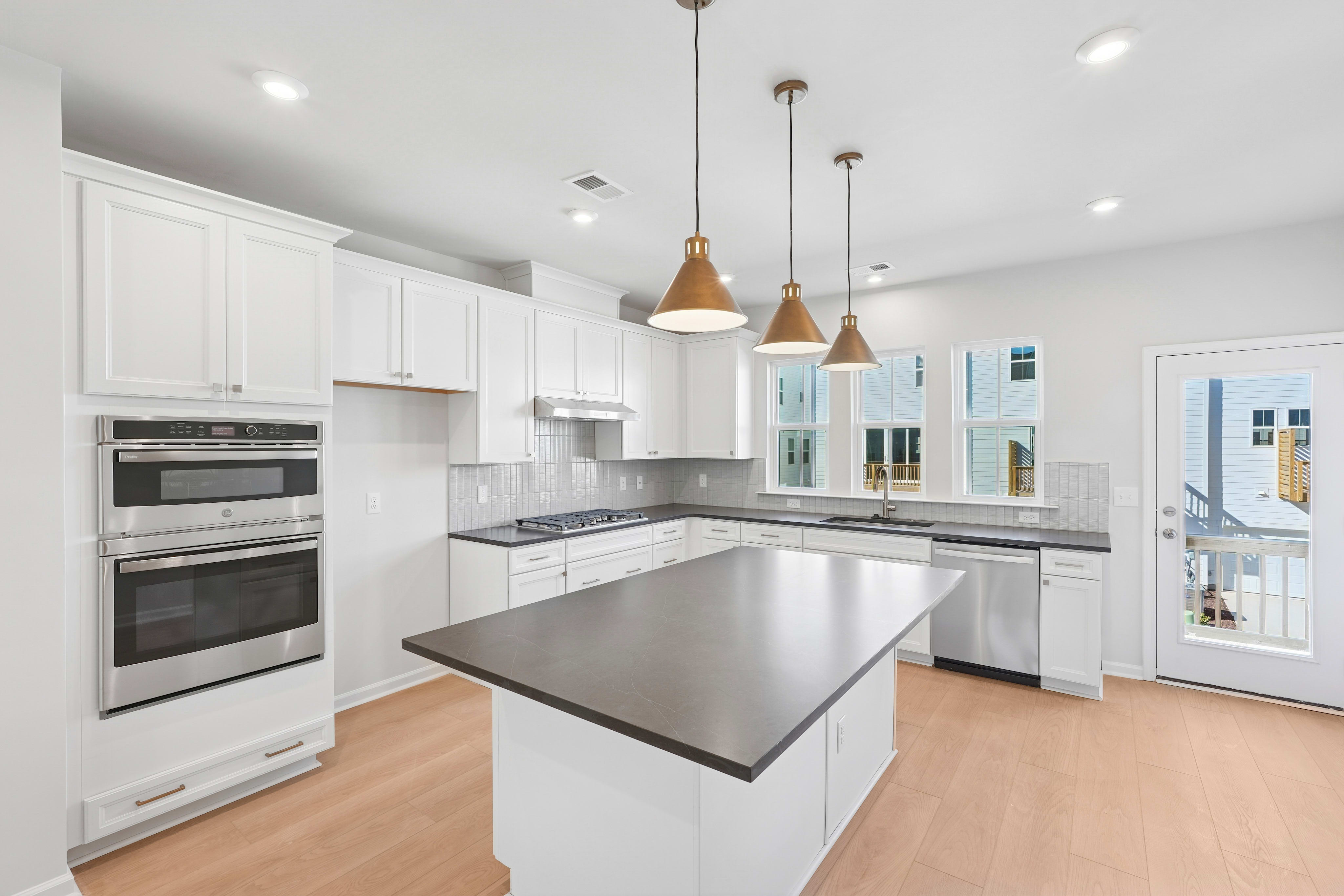 A modern, well-lit kitchen with white cabinets, stainless steel appliances, and a central island with a gray countertop.