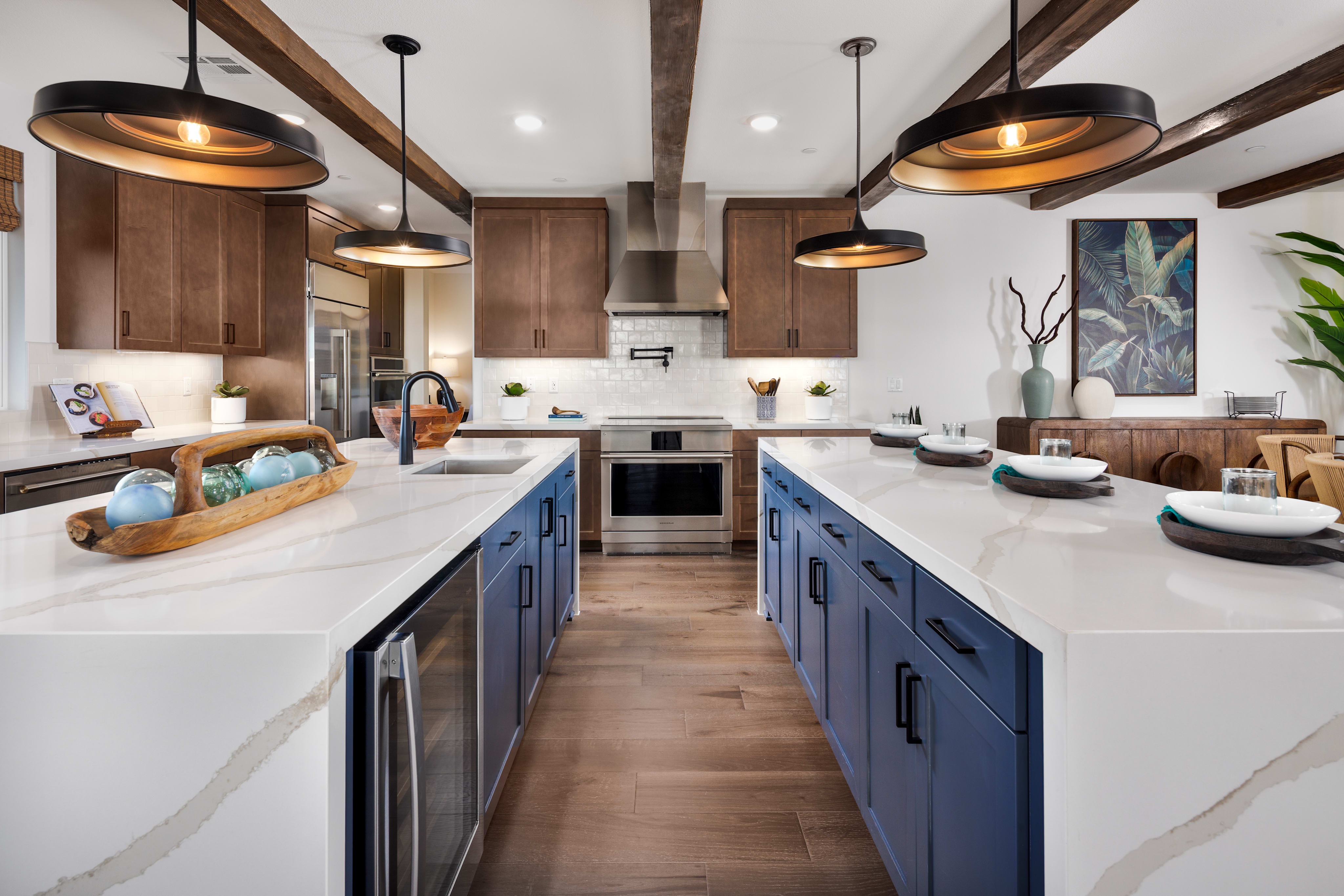 A modern and stylish kitchen with wooden beams, blue cabinets, and pendant lights, featuring a central island and various kitchen appliances and decor.