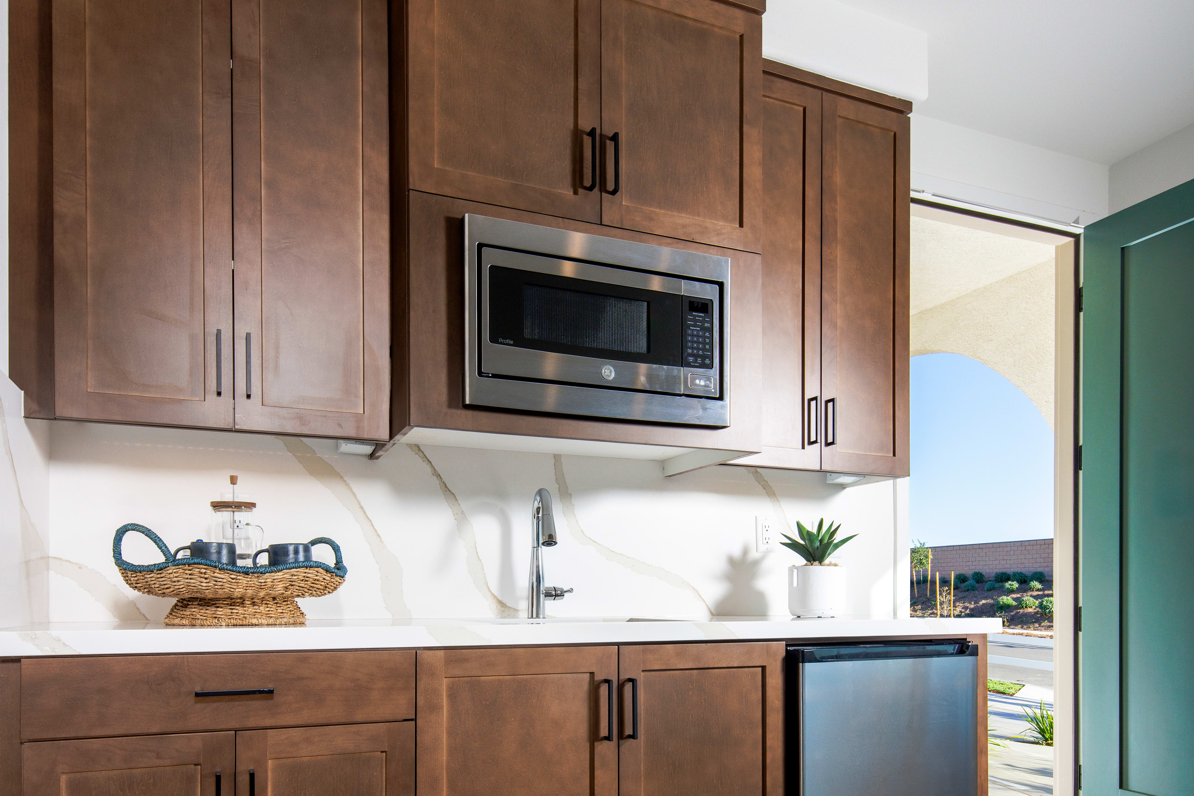 A modern kitchen with wooden cabinets, a stainless steel appliance, and a view of the outdoors through a sliding glass door.