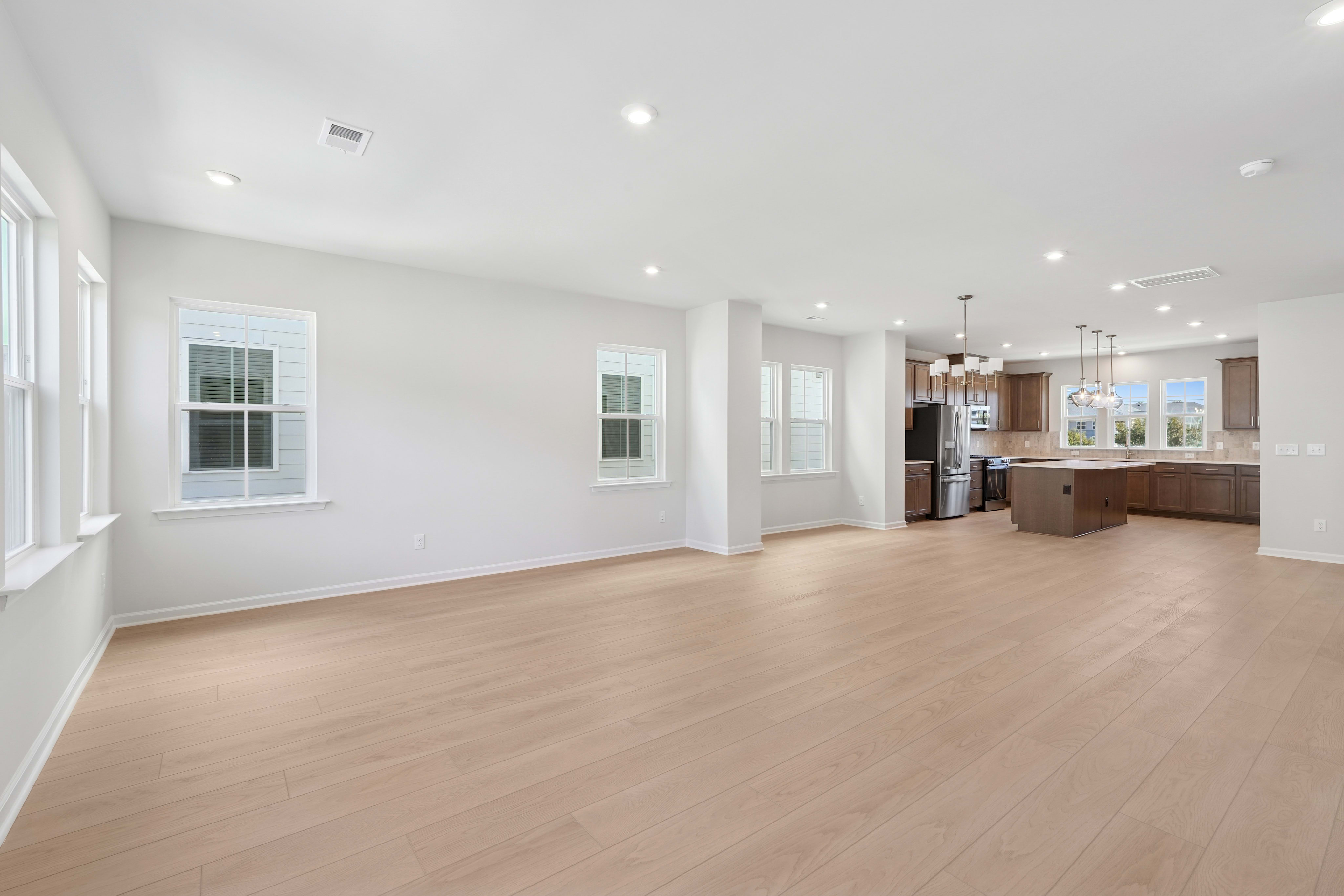 A spacious and bright open-concept living area with hardwood floors, large windows, and a modern kitchen visible in the background.