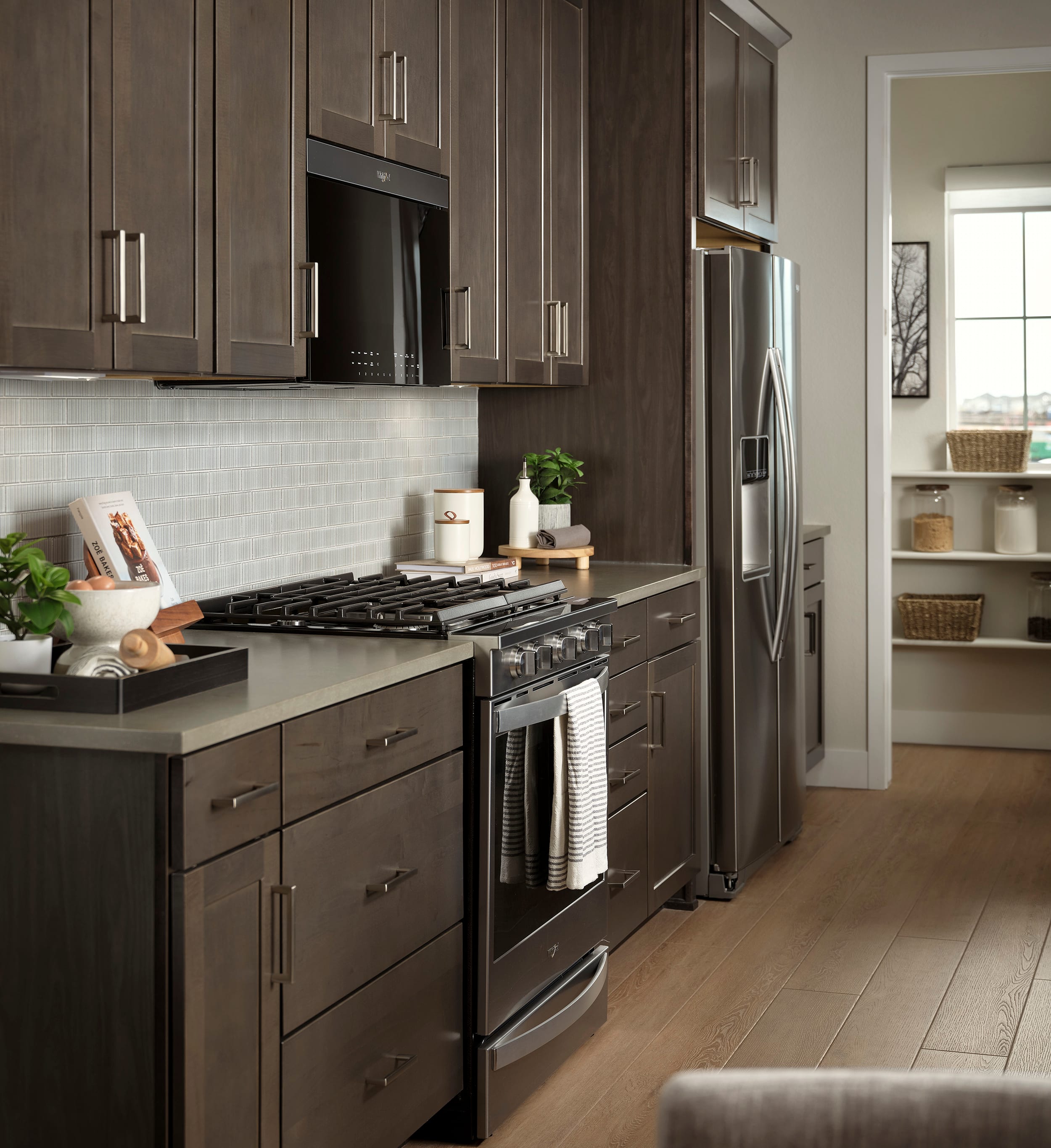 A modern, well-equipped kitchen with dark wood cabinets, stainless steel appliances, and a tiled backsplash, set against a light-colored hardwood floor.