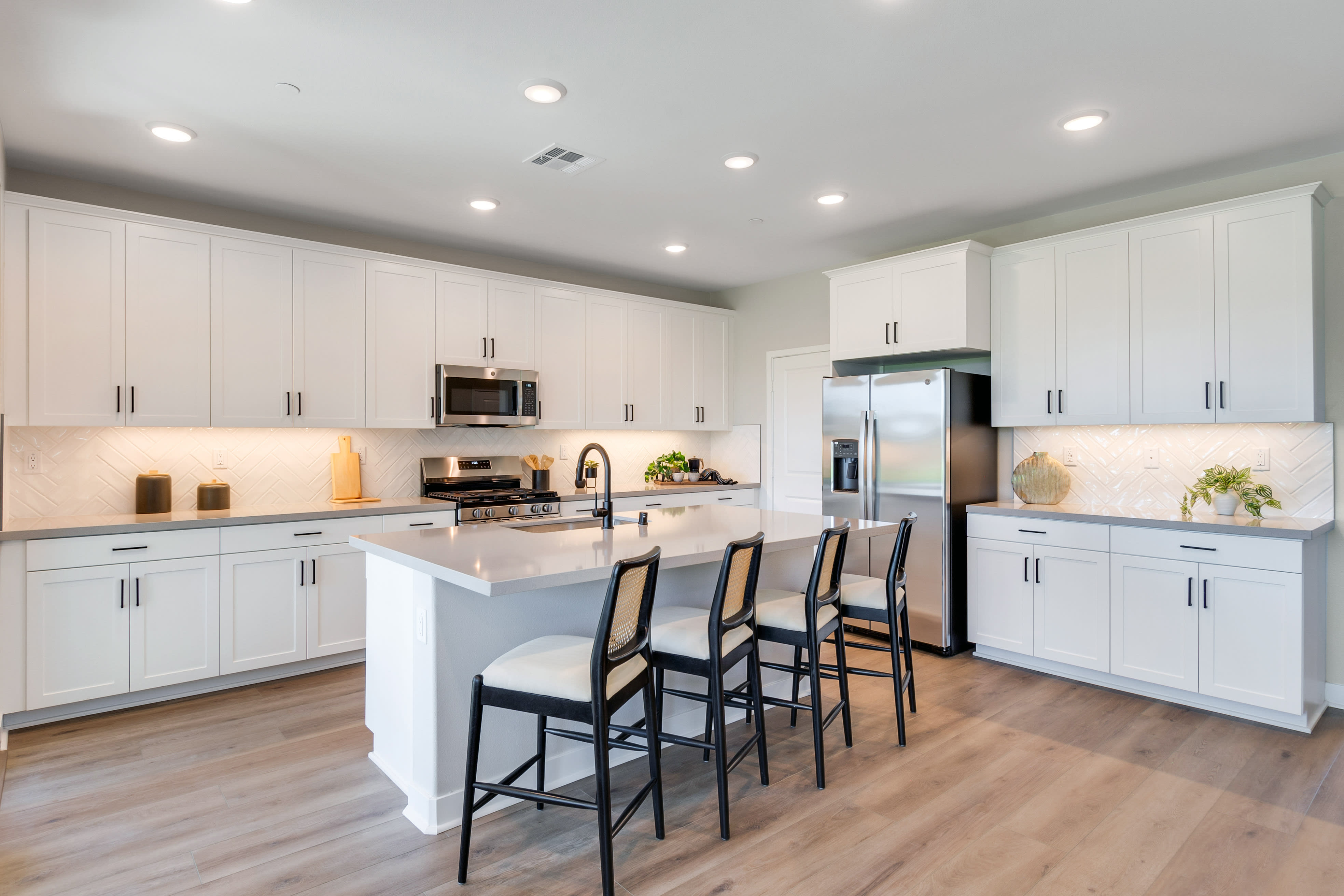A modern, well-lit kitchen with white cabinets, a center island, and hardwood floors.