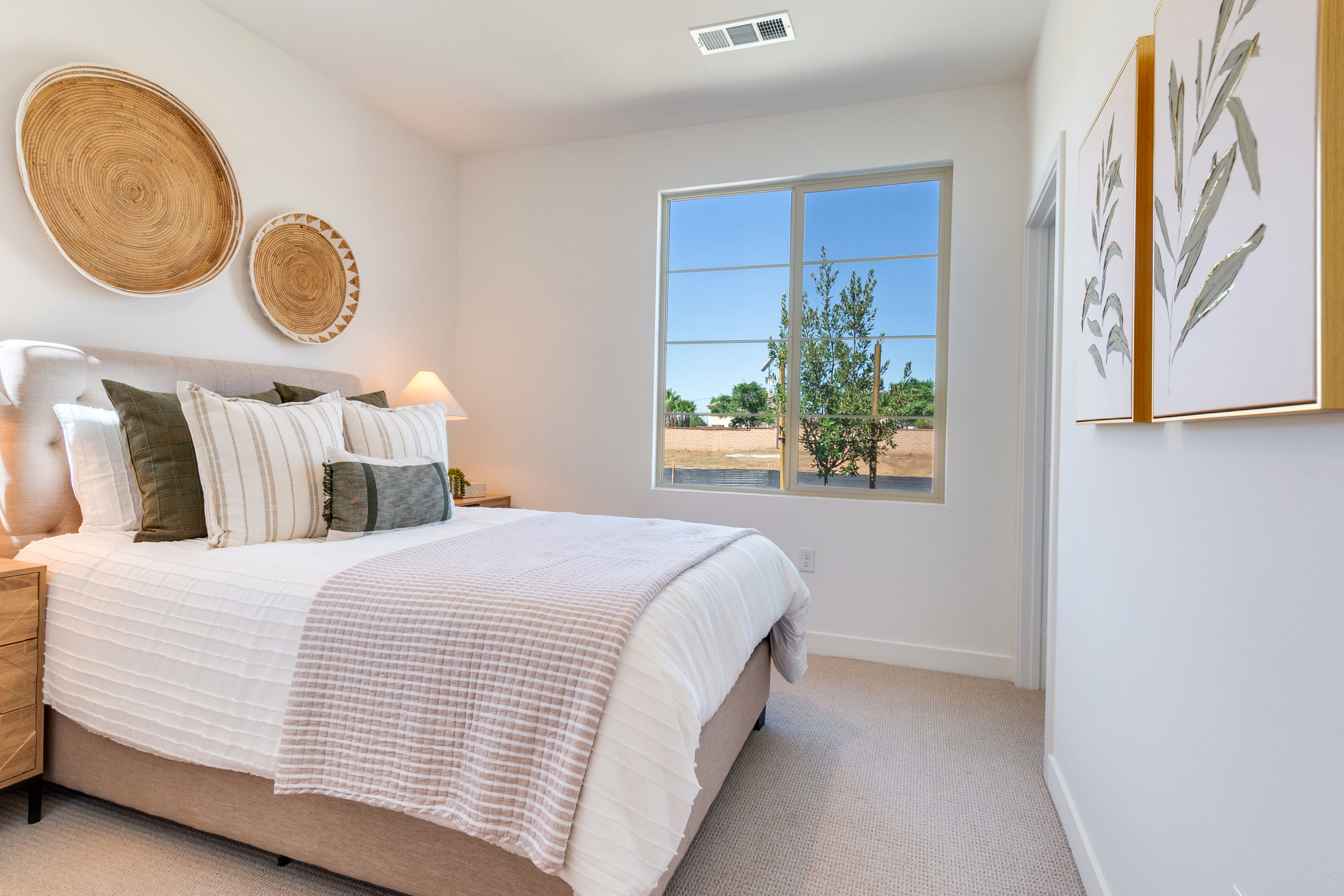 A cozy and inviting bedroom with a large window overlooking a lush outdoor landscape, featuring a plush bed adorned with neutral-toned bedding and decorative wall art.