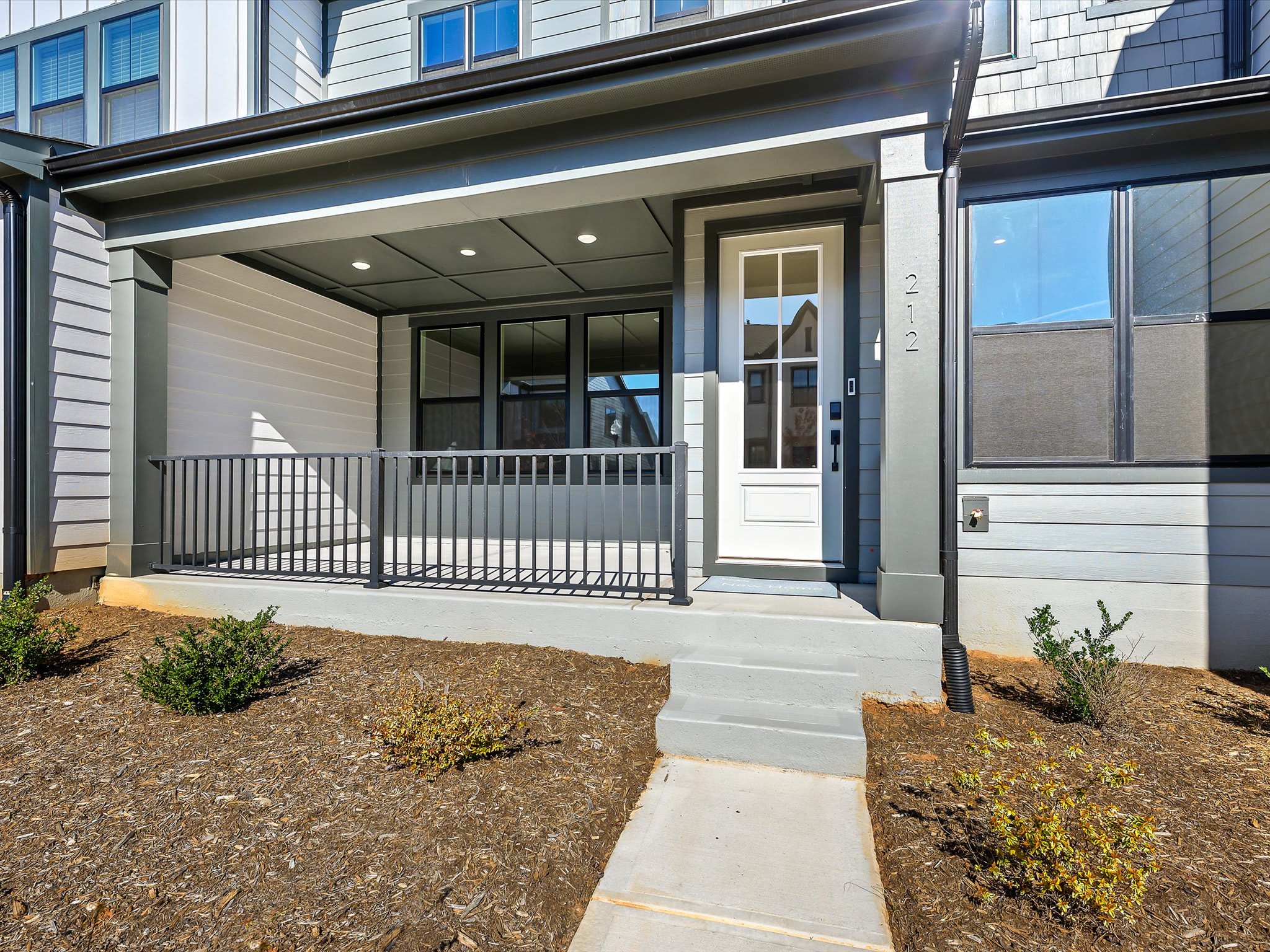 A modern, two-story residential building with a covered porch, surrounded by a landscaped yard with a paved walkway leading to the entrance.