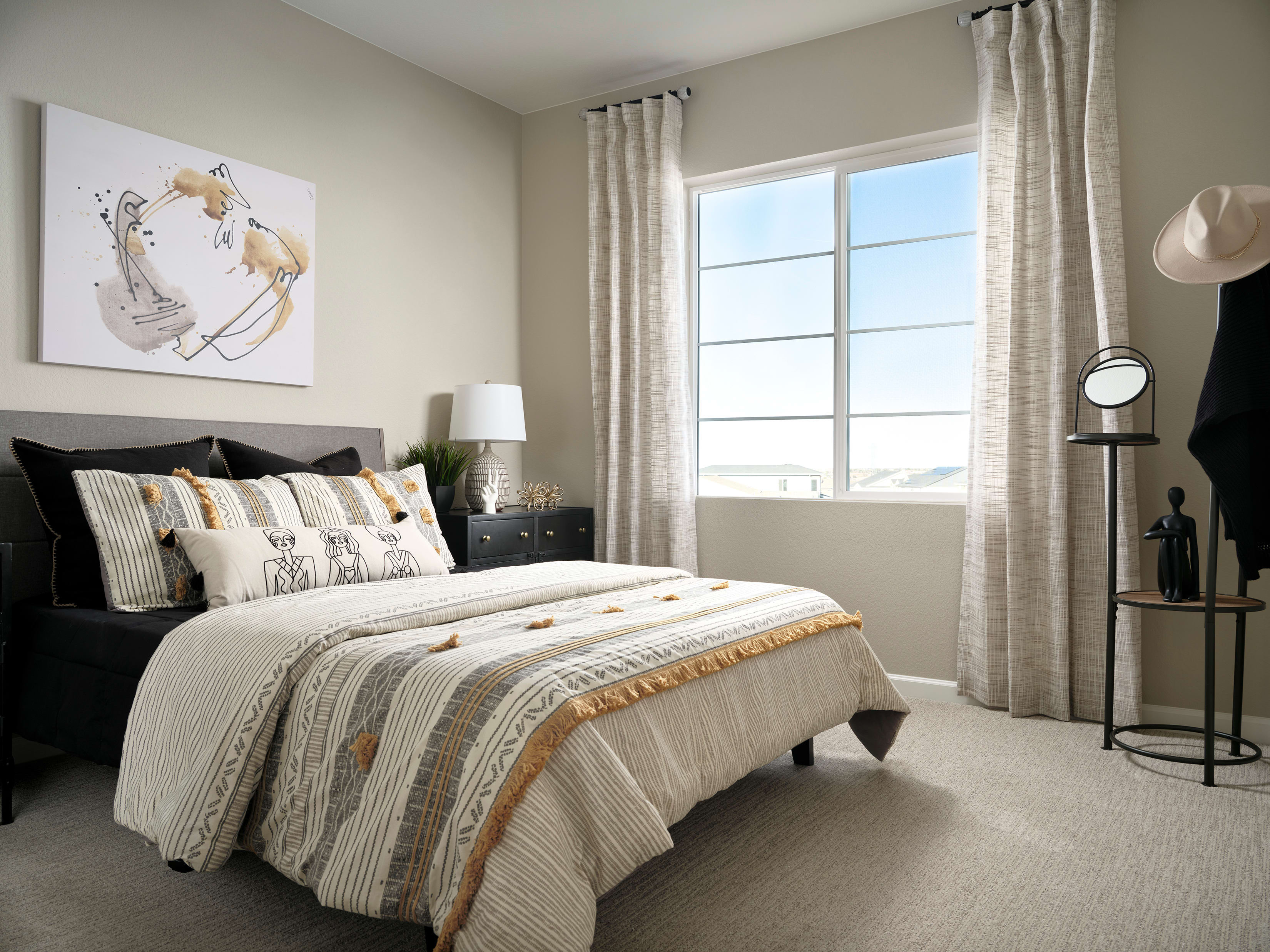 A cozy and well-decorated bedroom with a large window, a black bed frame, and a patterned bedspread, along with various decorative elements such as lamps and artwork on the walls.