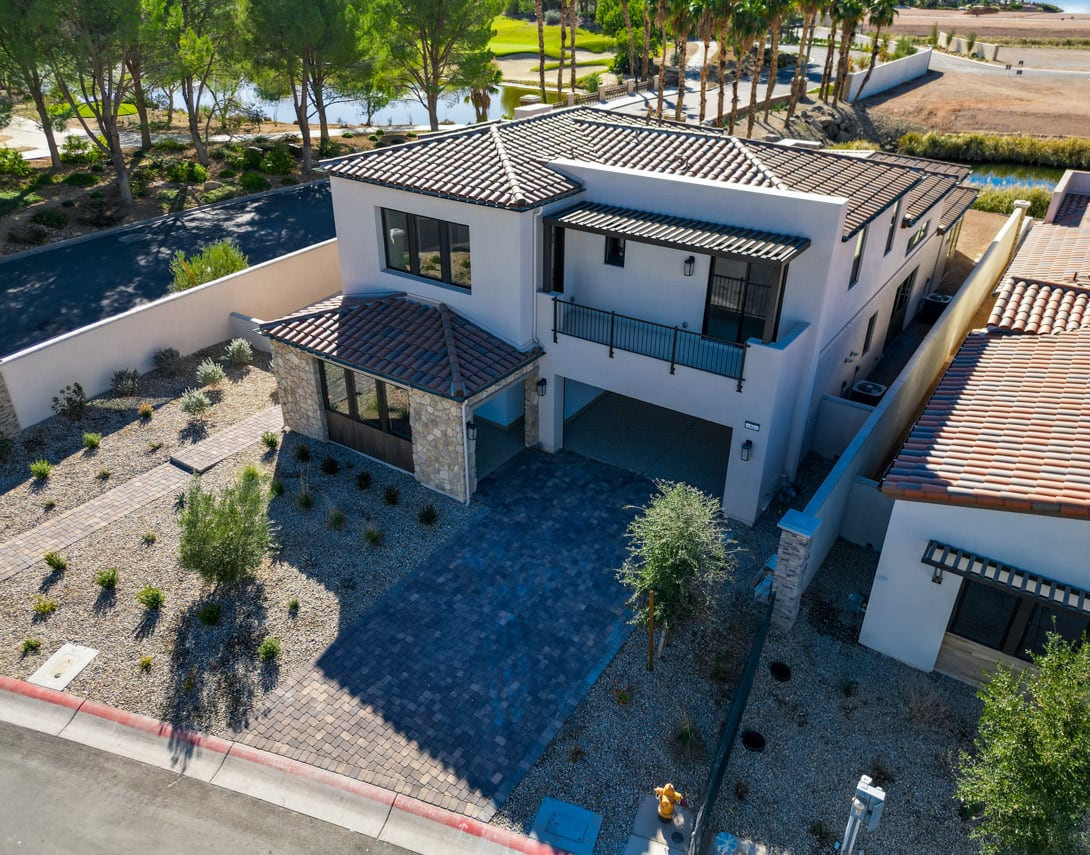 A large, two-story Mediterranean-style villa with a tiled roof, surrounded by a lush, landscaped garden and a swimming pool in the foreground.