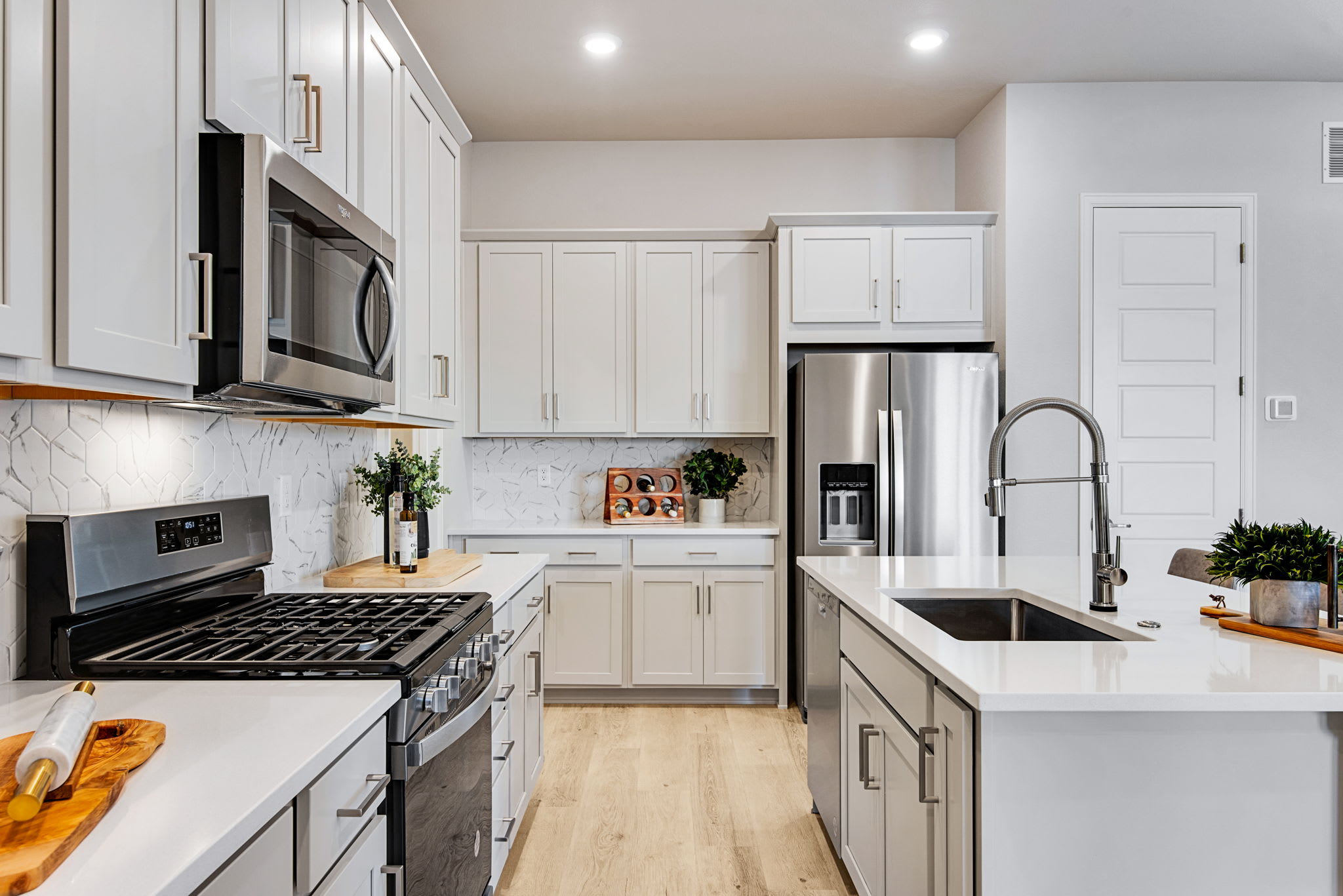 A modern, well-equipped kitchen with white cabinets, stainless steel appliances, and a marble countertop, featuring a gas stove, microwave, and a sink with a faucet.