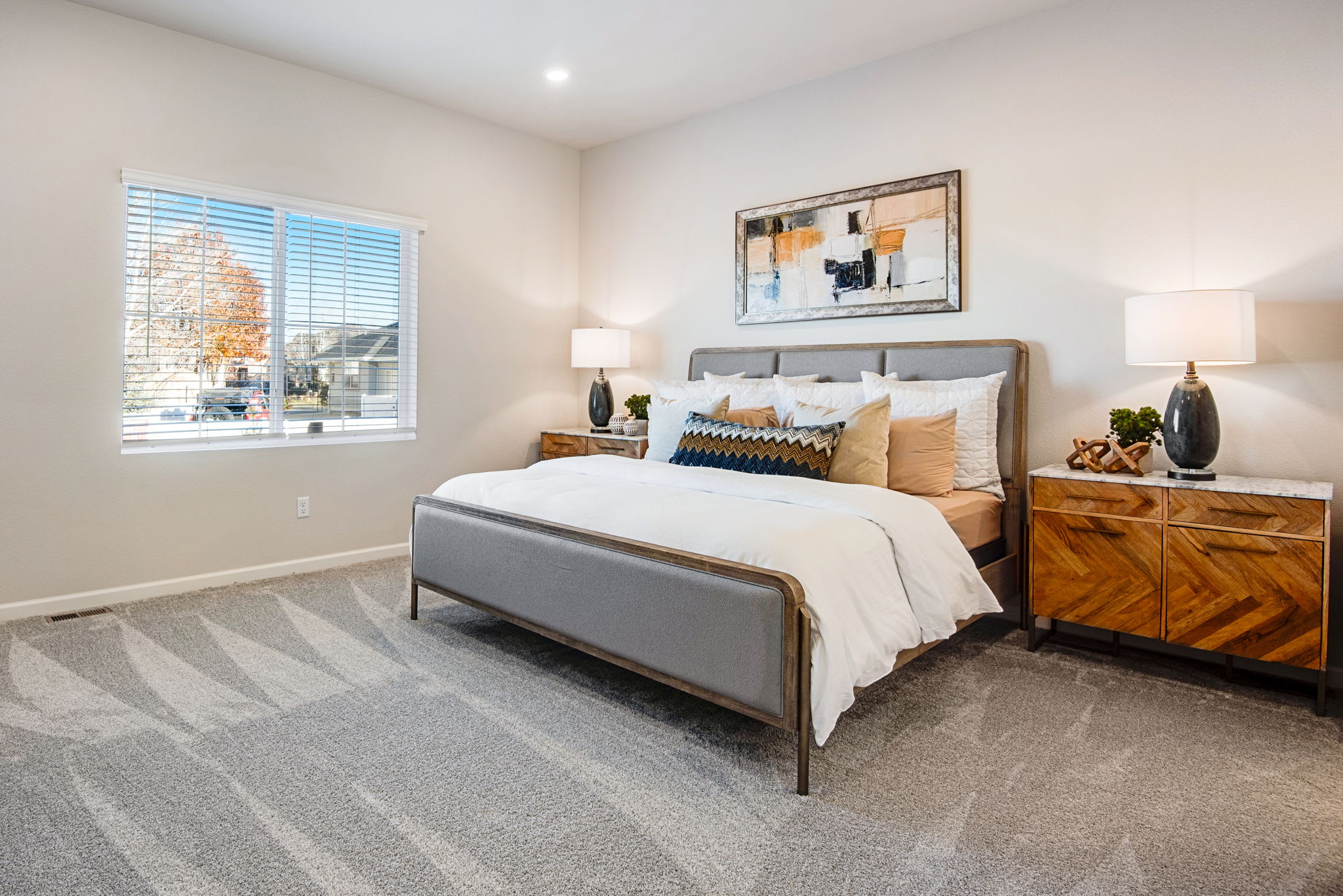 A cozy and well-furnished bedroom with a large bed, wooden dresser, and artwork on the wall, set against a backdrop of a bright window and neutral-toned walls.