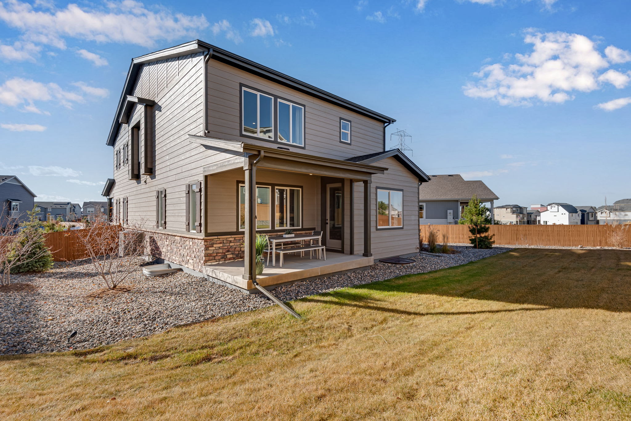 A two-story modern house with a porch, surrounded by a grassy yard and a clear blue sky with scattered clouds in the background.