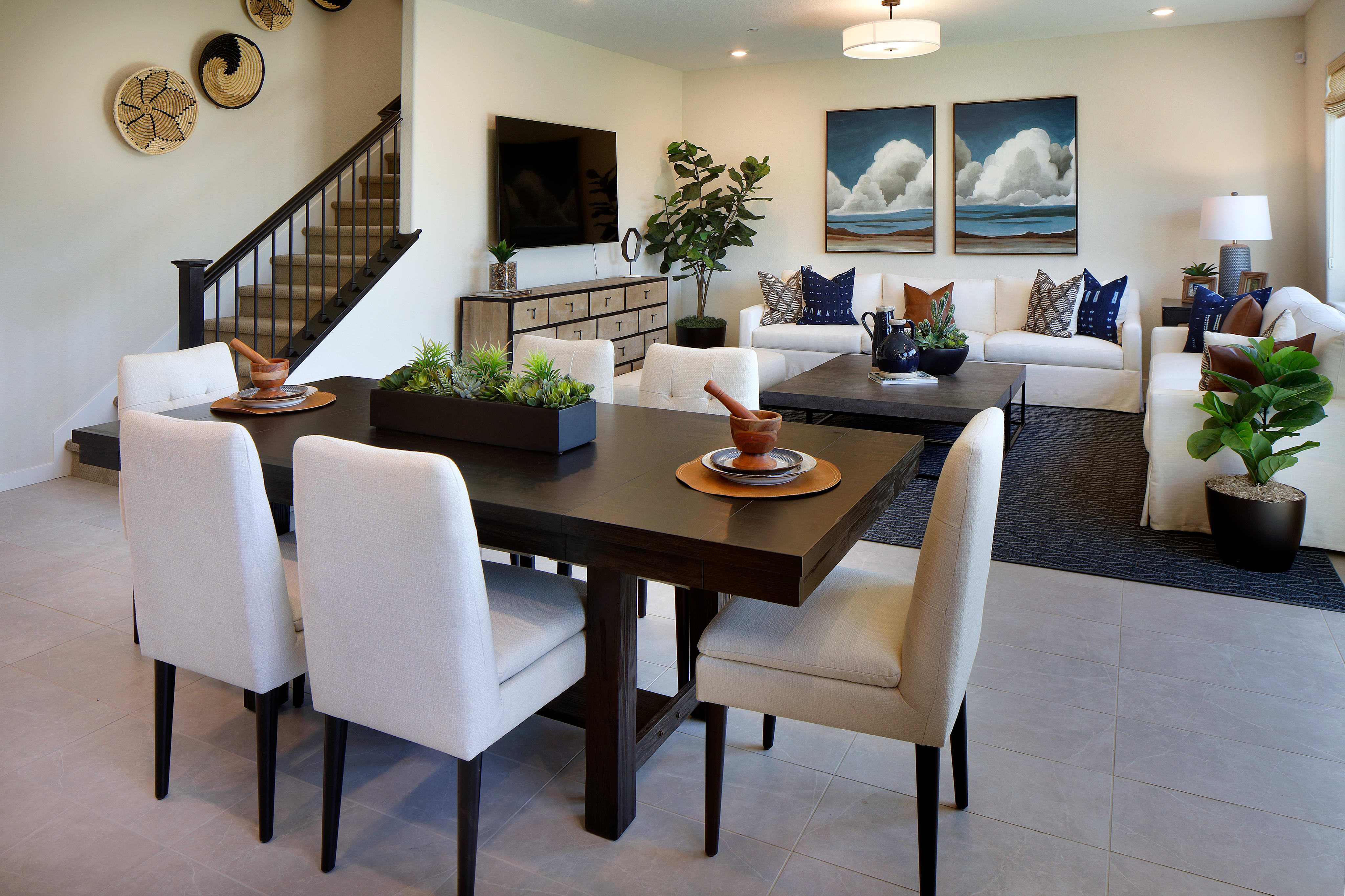 A modern and stylish living room with a dining area, featuring a dark wooden table surrounded by white chairs, and a cozy seating arrangement with plush sofas and decorative accents.