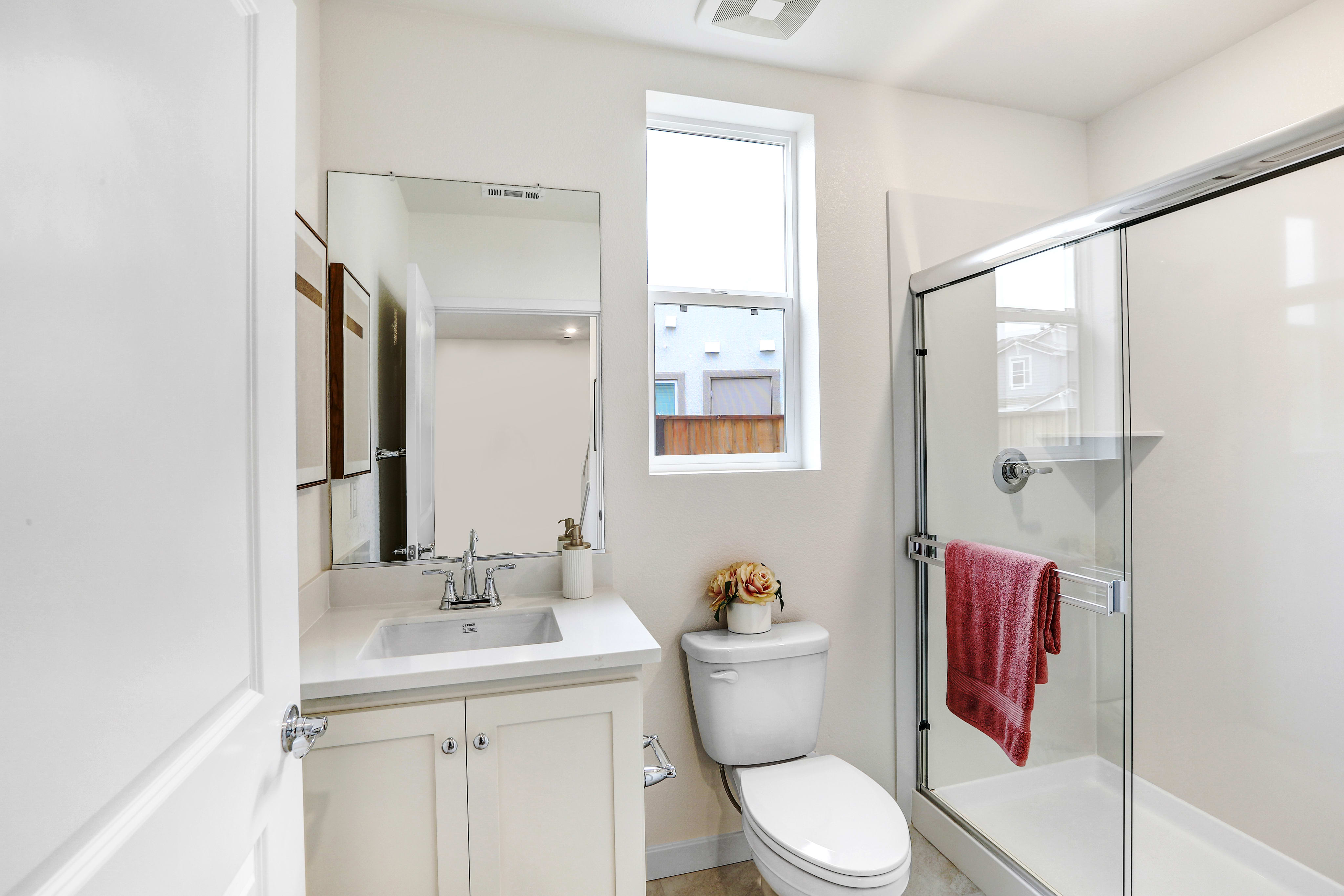 A bright and clean bathroom with a vanity, toilet, and glass-enclosed shower, featuring a small decorative item on the vanity.