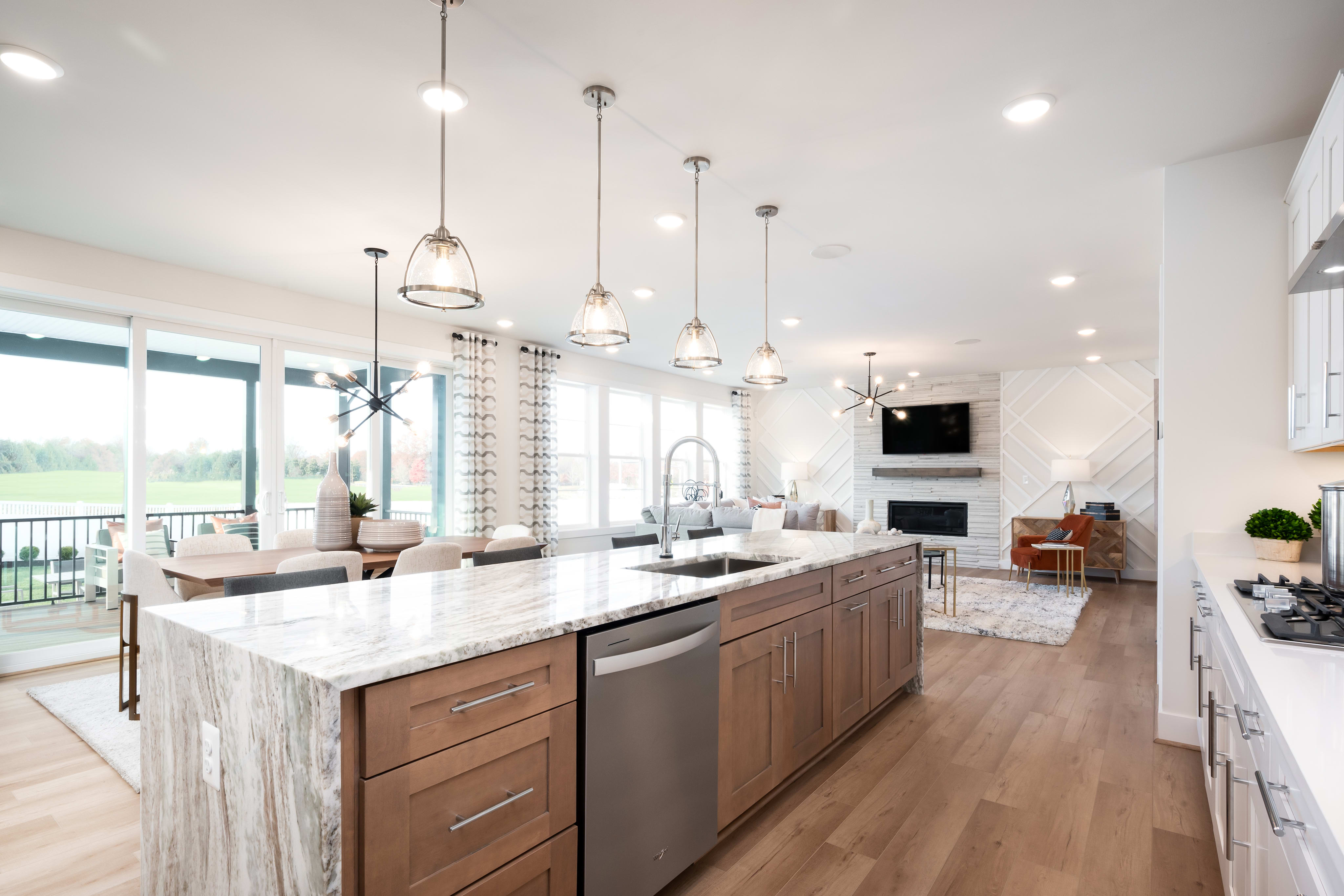 A modern, open-concept kitchen with a large island, pendant lighting, and a view of the surrounding landscape through large windows.