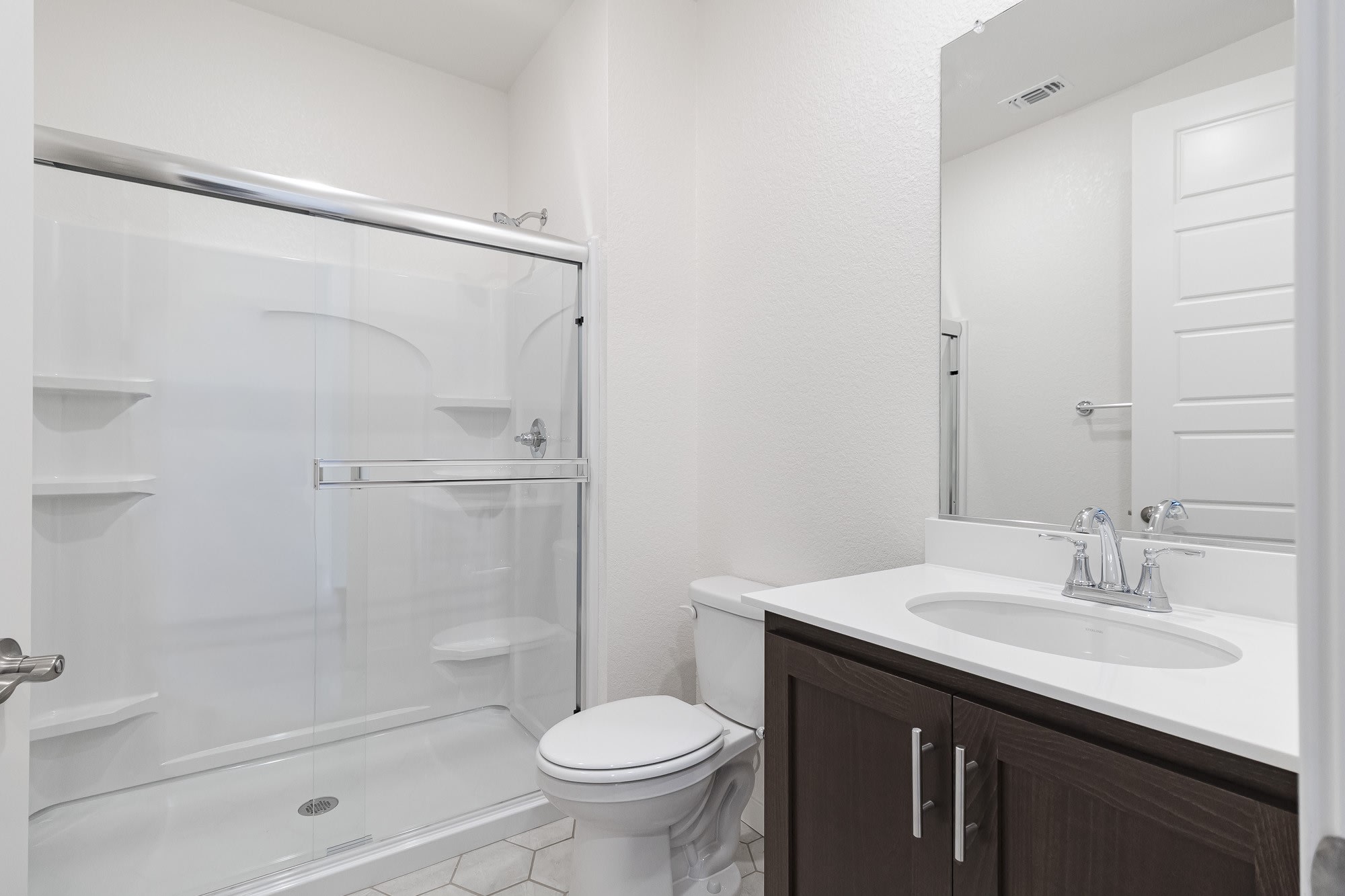 A modern, minimalist bathroom with a white vanity, a toilet, and a glass-enclosed shower stall, all set against a clean, bright backdrop.