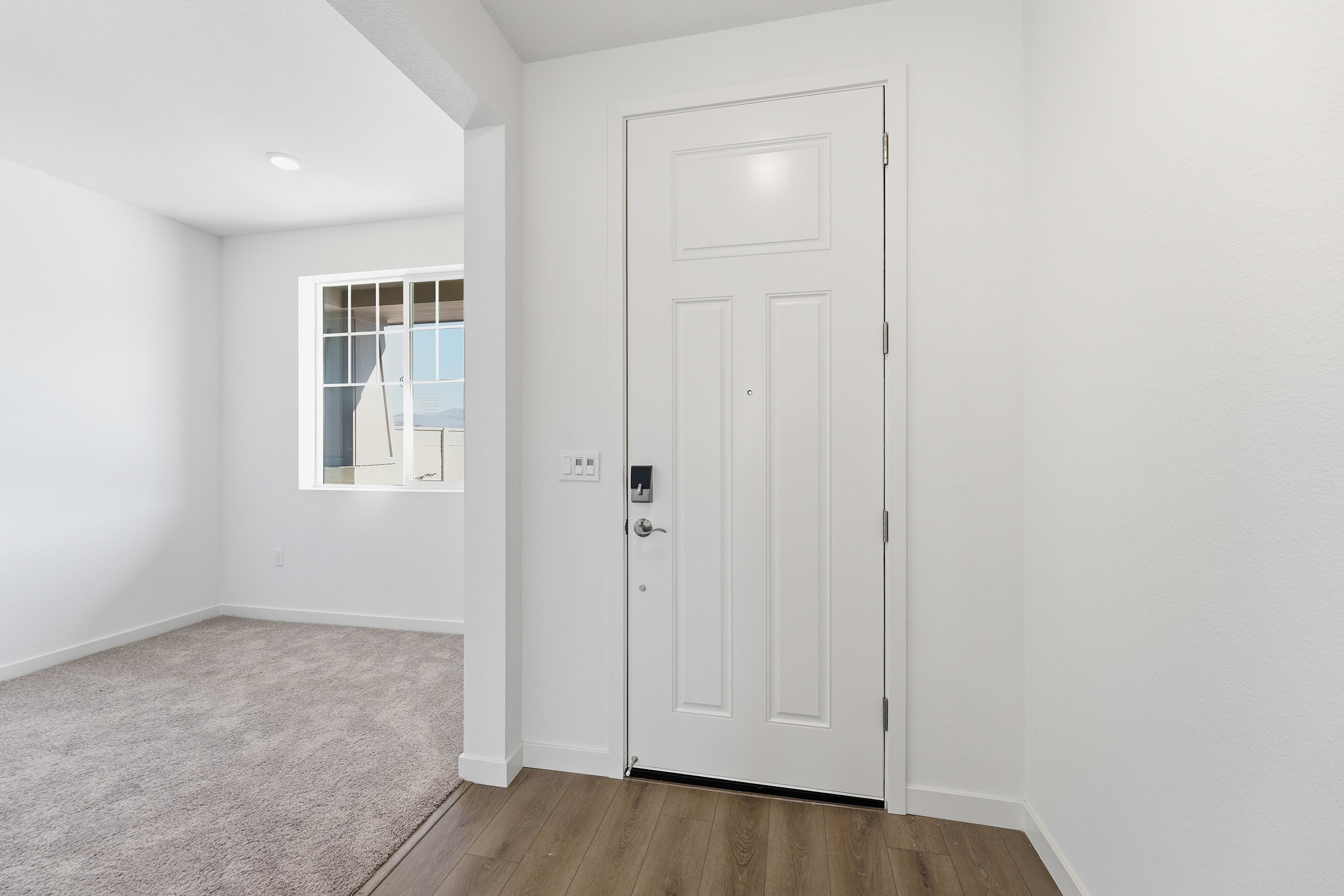 A bright, minimalist room with a white door, hardwood flooring, and a window providing natural light.