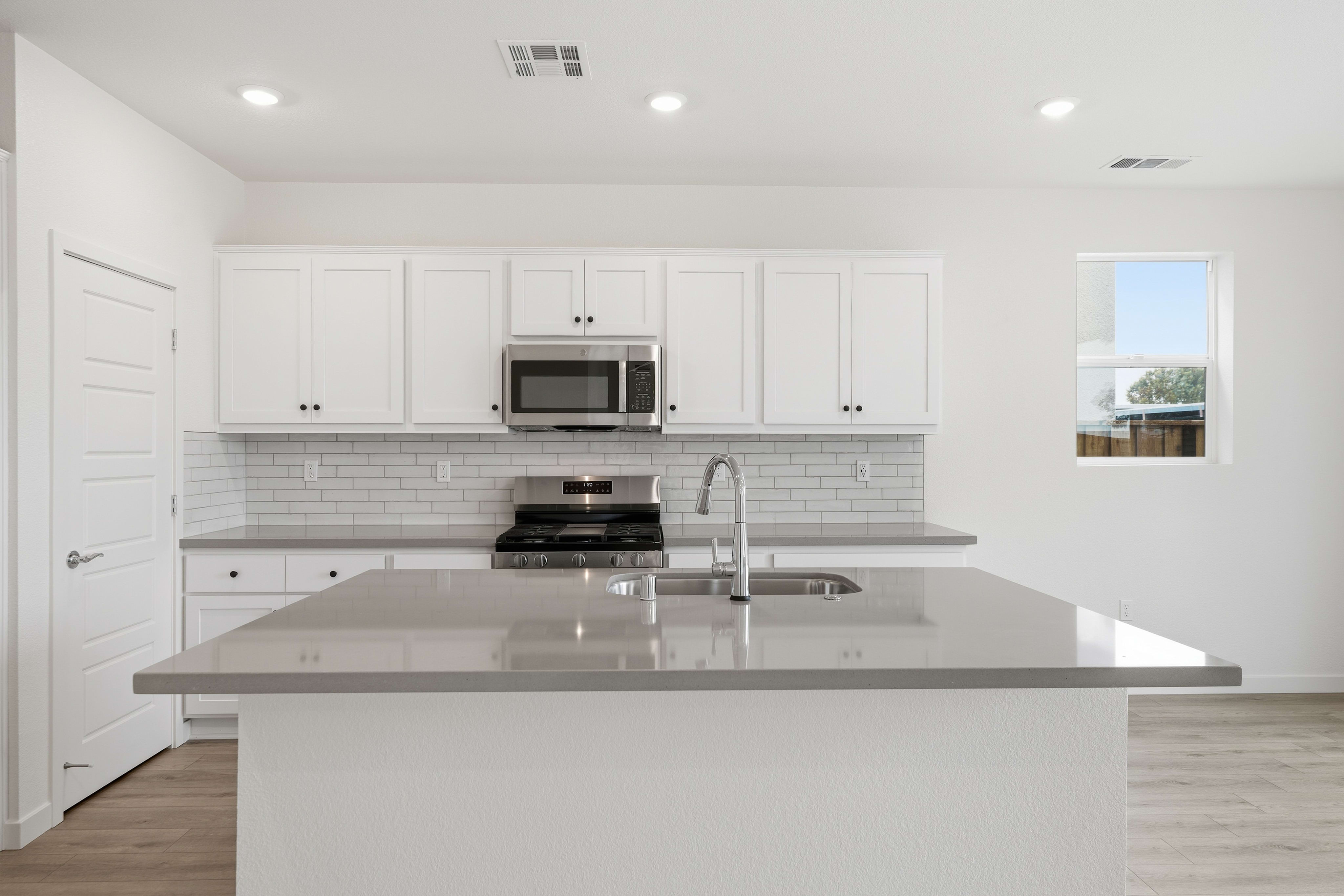 A modern, bright kitchen with white cabinets, gray countertops, and a stainless steel appliance in the background.