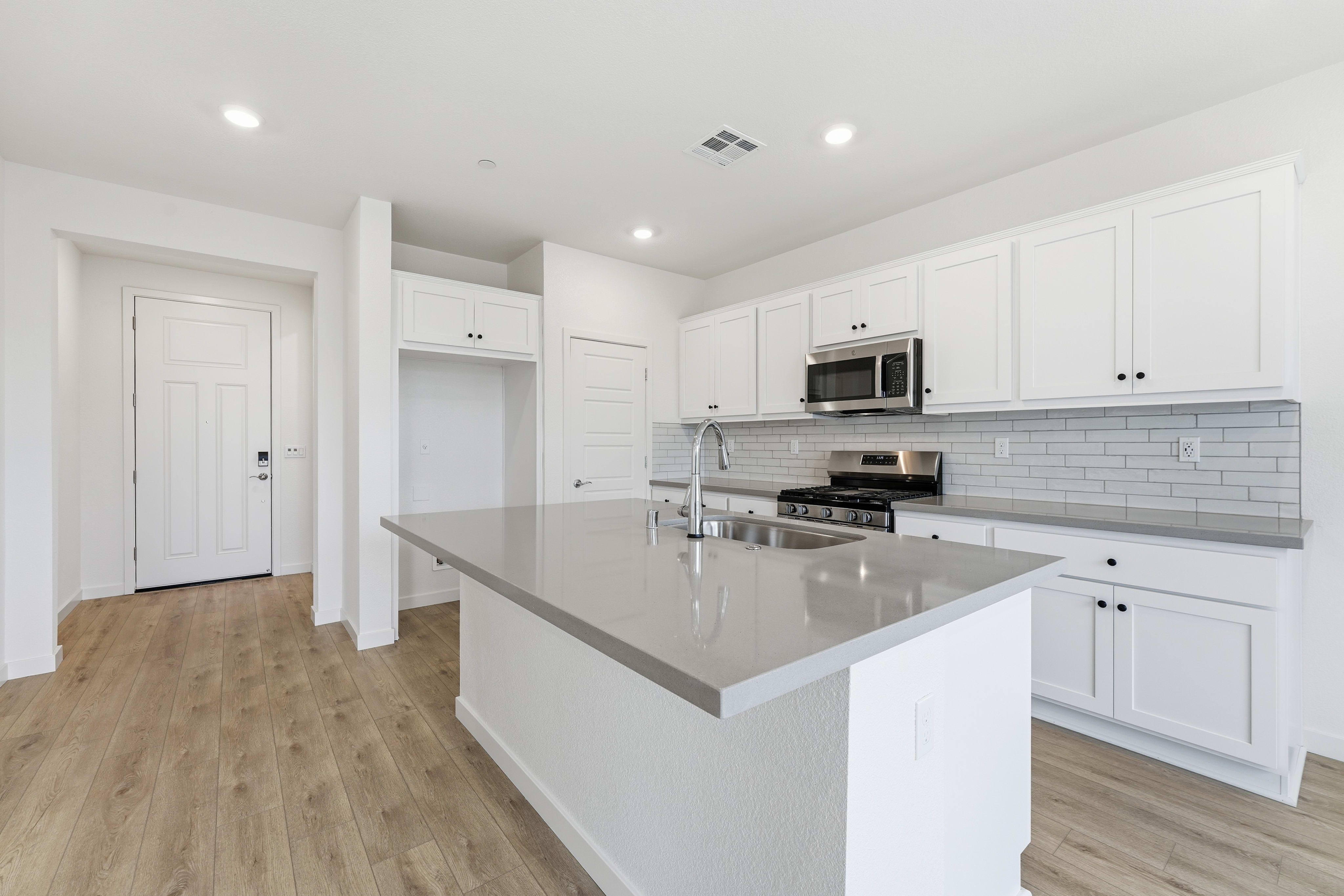 A modern, bright kitchen with white cabinets, gray countertops, and a hardwood floor.
