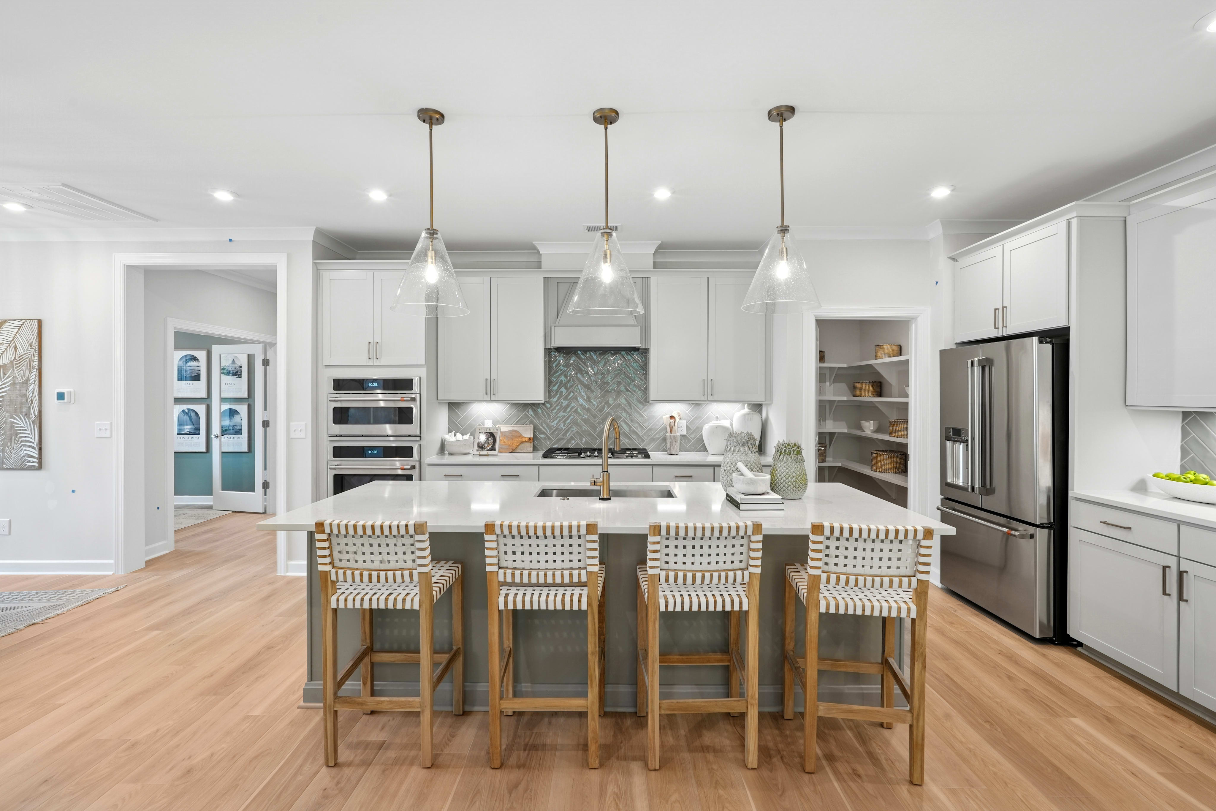 A modern, open-concept kitchen with white cabinets, stainless steel appliances, a large island with bar stools, and pendant lighting fixtures.