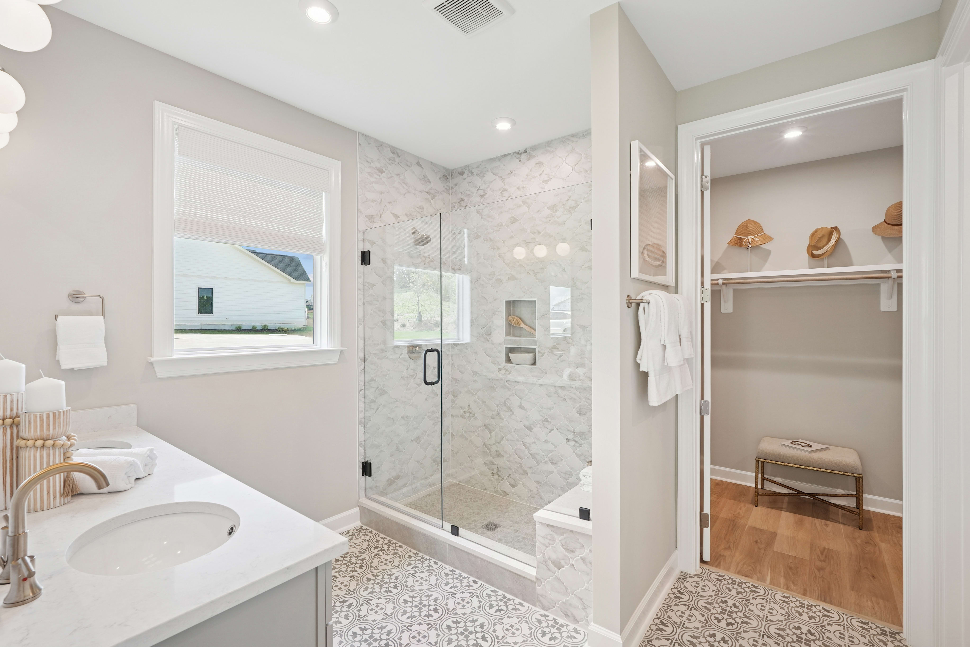 A modern, well-designed bathroom with a glass-enclosed shower, a vanity with a white countertop, and a closet area visible in the background.