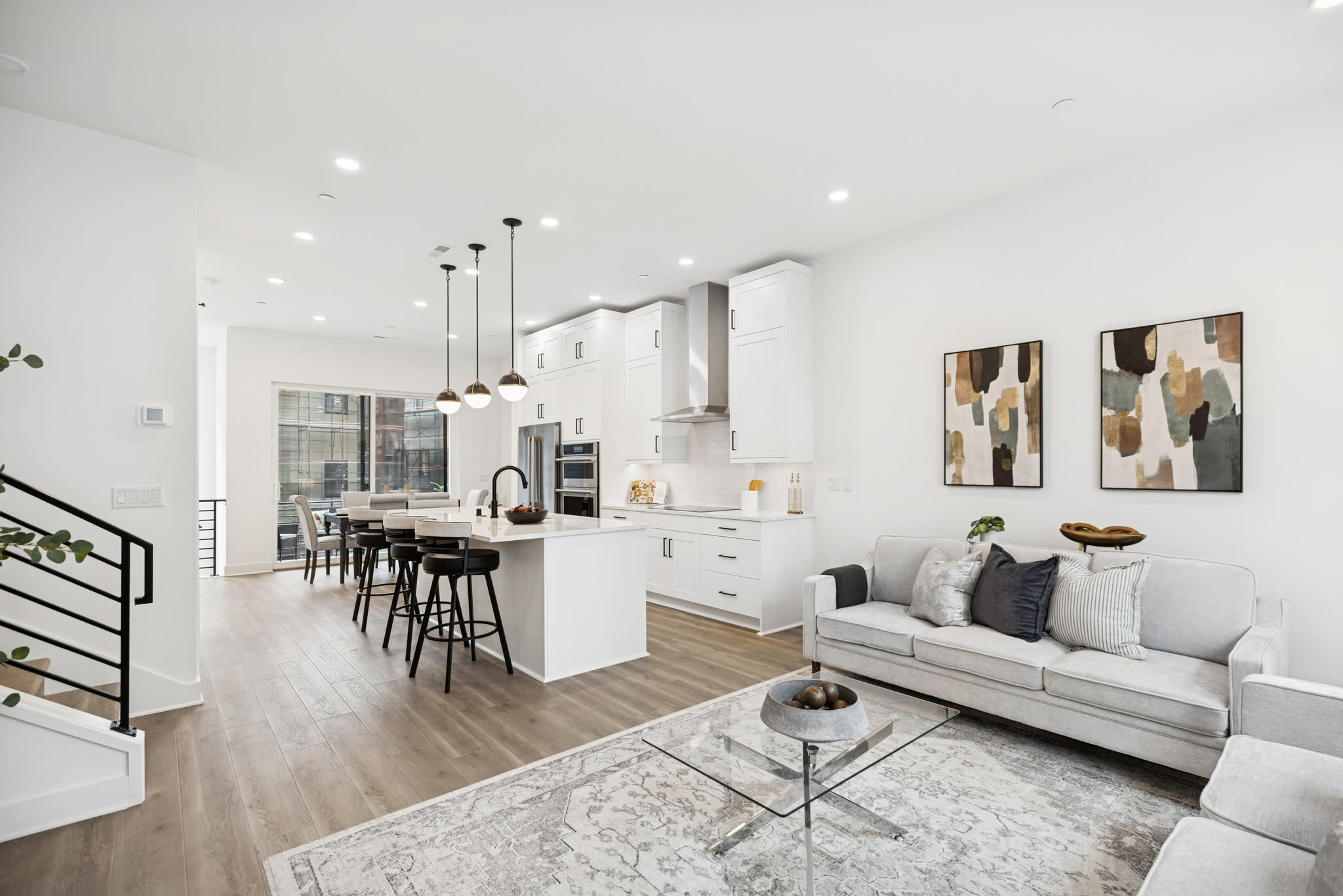 A modern, open-concept living space with a white kitchen, a gray sofa, and abstract artwork on the walls.