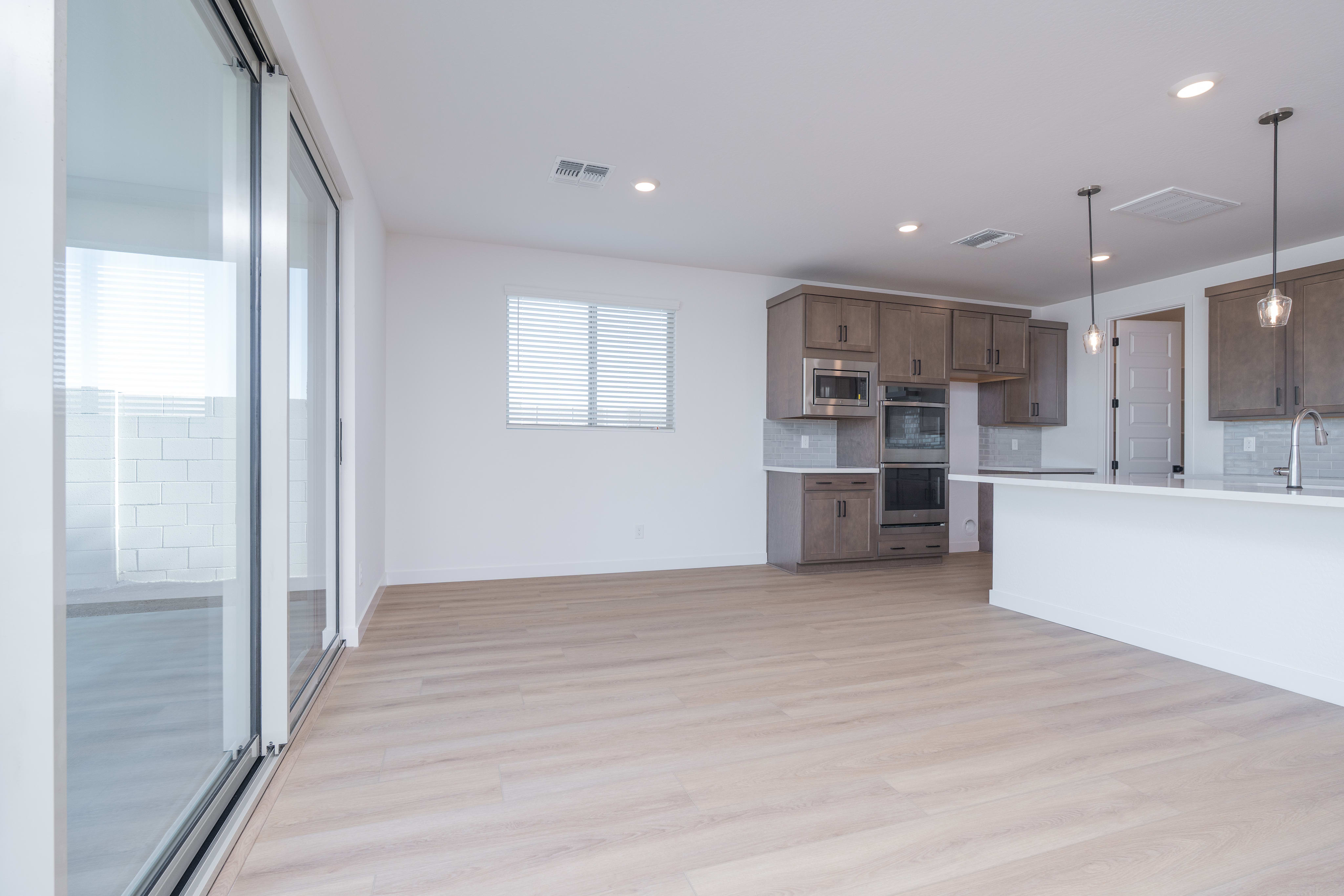 A modern, open-concept kitchen and living space with light-colored wood flooring, white walls, and a large sliding glass door leading to an outdoor area.