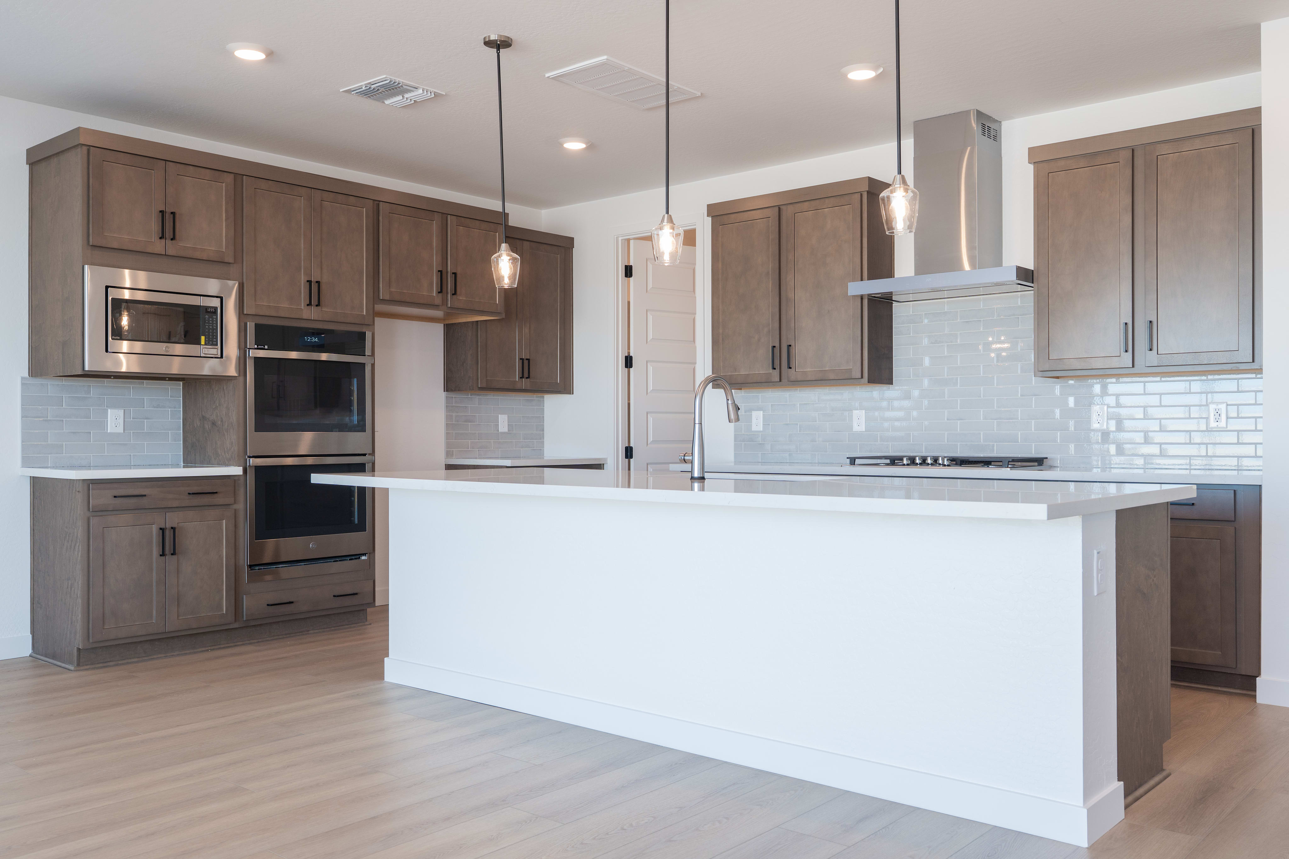 A modern, open-concept kitchen with light wood cabinets, a white island, and stainless steel appliances, set against a backdrop of hardwood floors.