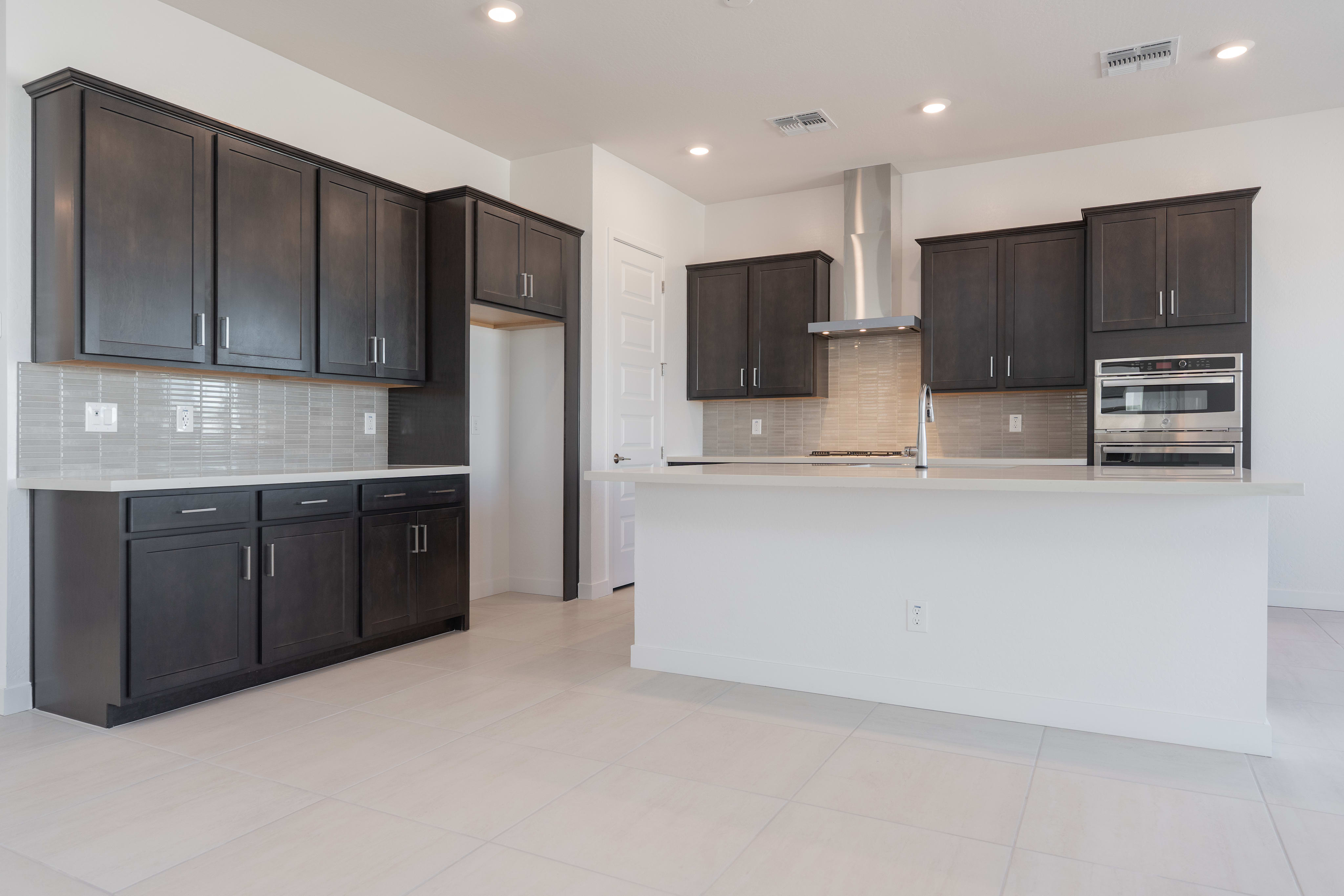 A modern, open-concept kitchen with dark wood cabinets, white countertops, and stainless steel appliances, set against a bright and airy background.