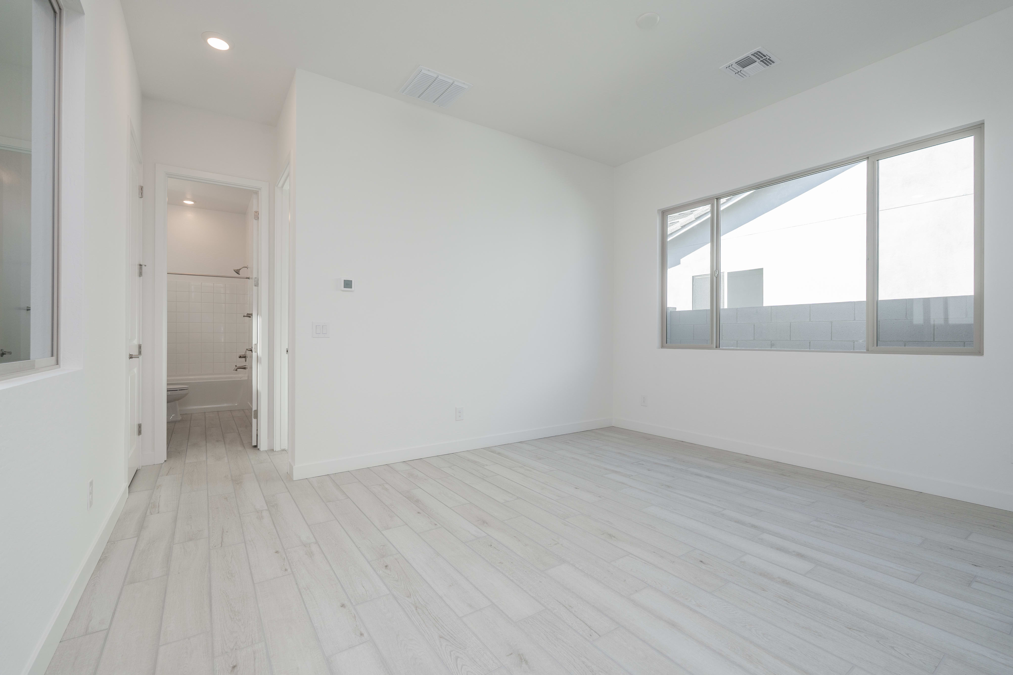 A bright, minimalist room with white walls, a hardwood floor, and a window providing natural light.