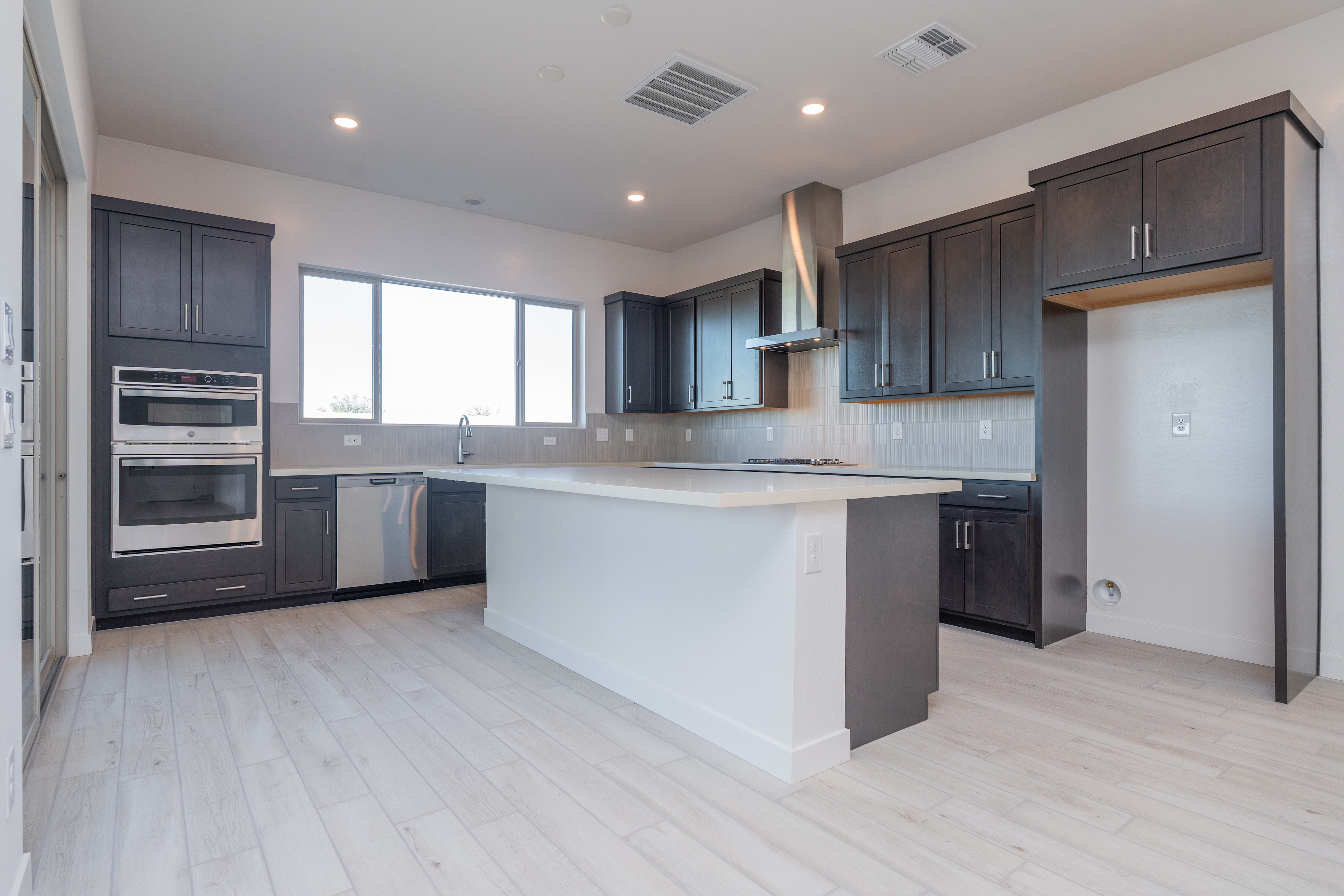 A modern, open-concept kitchen with dark cabinets, stainless steel appliances, and a white countertop island, set against a bright and airy background.