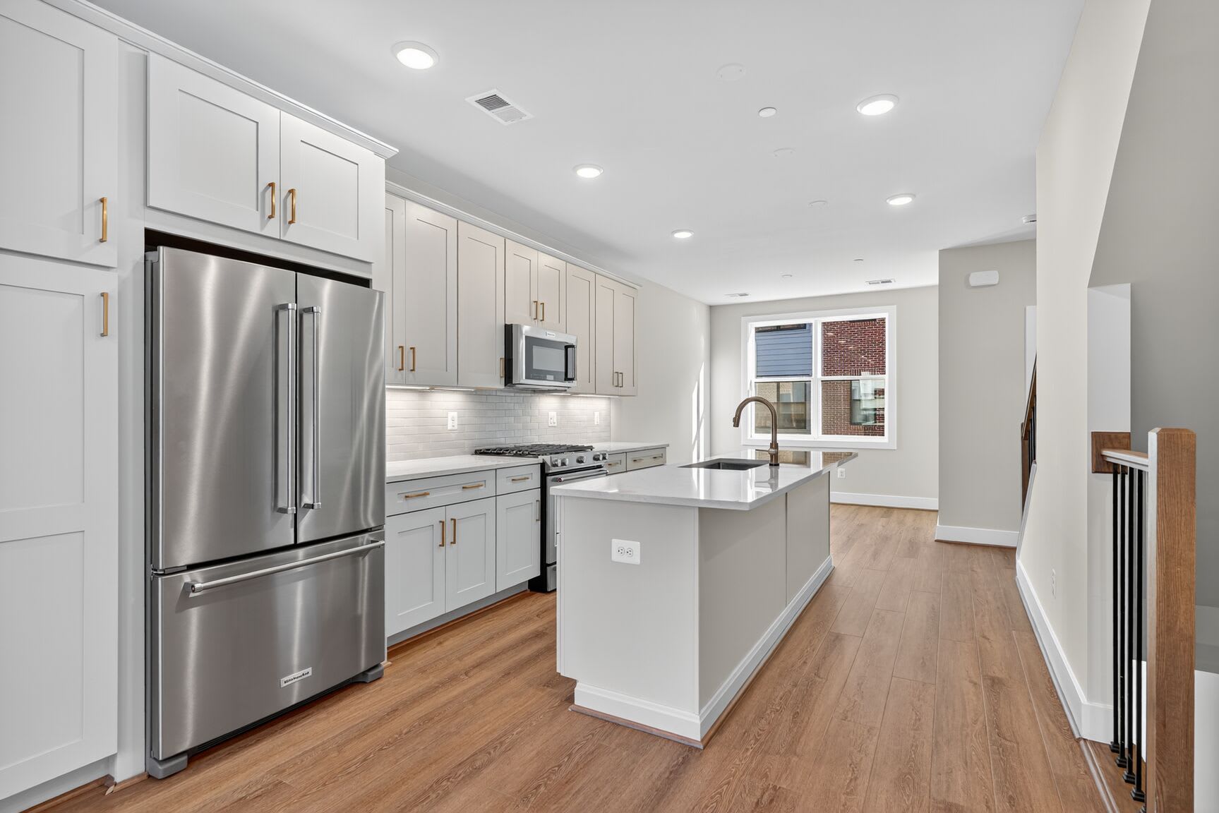 A modern, well-lit kitchen with white cabinets, stainless steel appliances, and a central island with a wooden countertop, set against a hardwood floor.