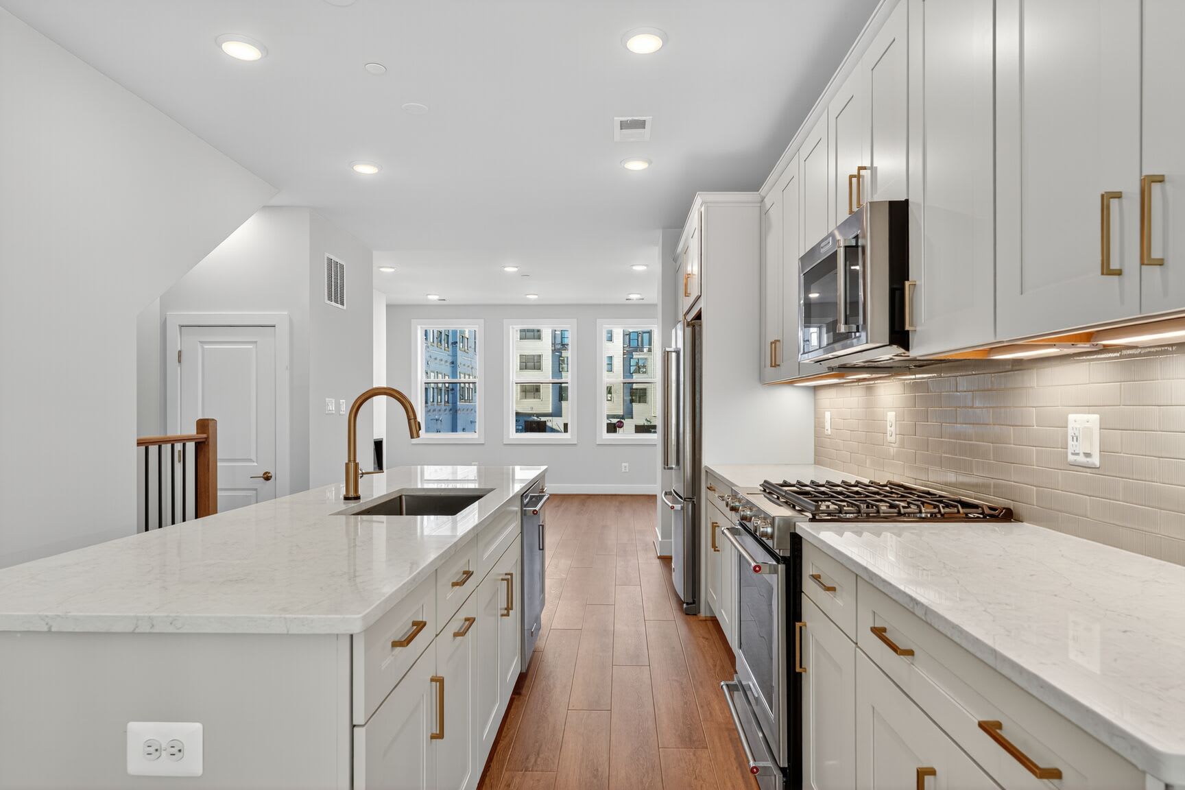 A modern, well-lit kitchen with white cabinets, stainless steel appliances, and a long countertop extending along the room's length.