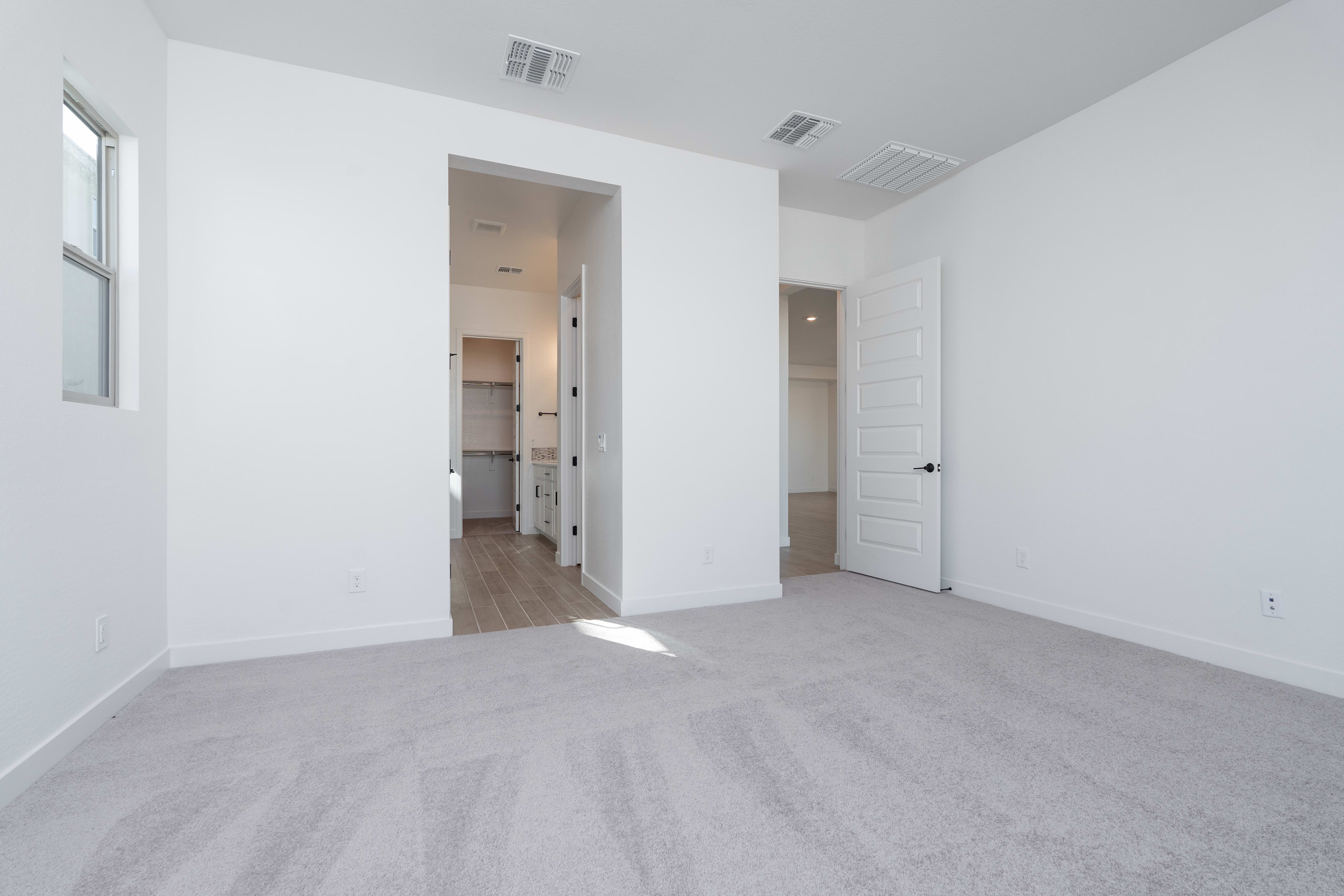 A spacious, minimalist room with white walls, hardwood floors, and two doorways leading to other areas of the space.