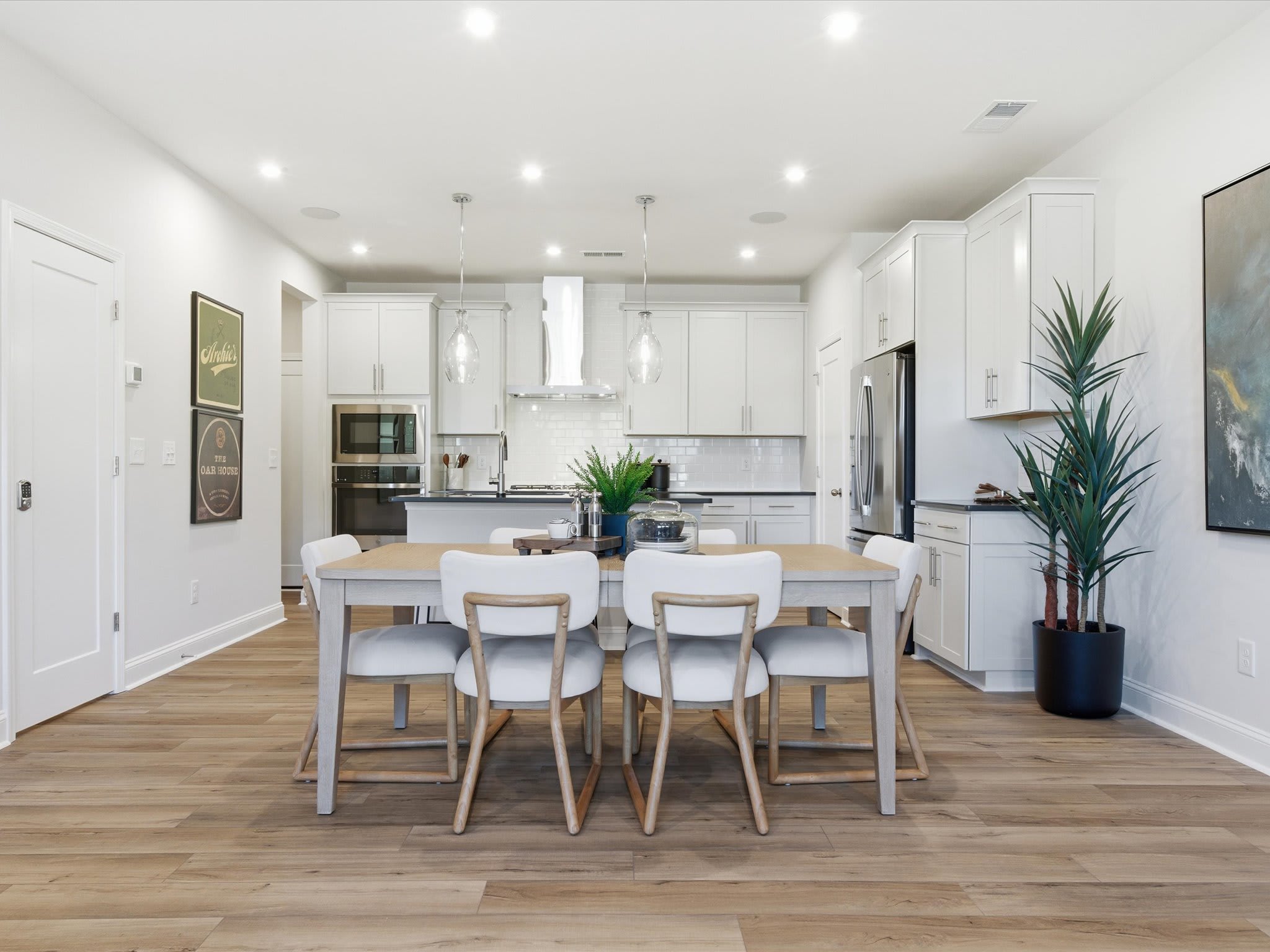 A modern, open-concept kitchen and dining area with white cabinets, stainless steel appliances, and a wooden dining table with chairs.