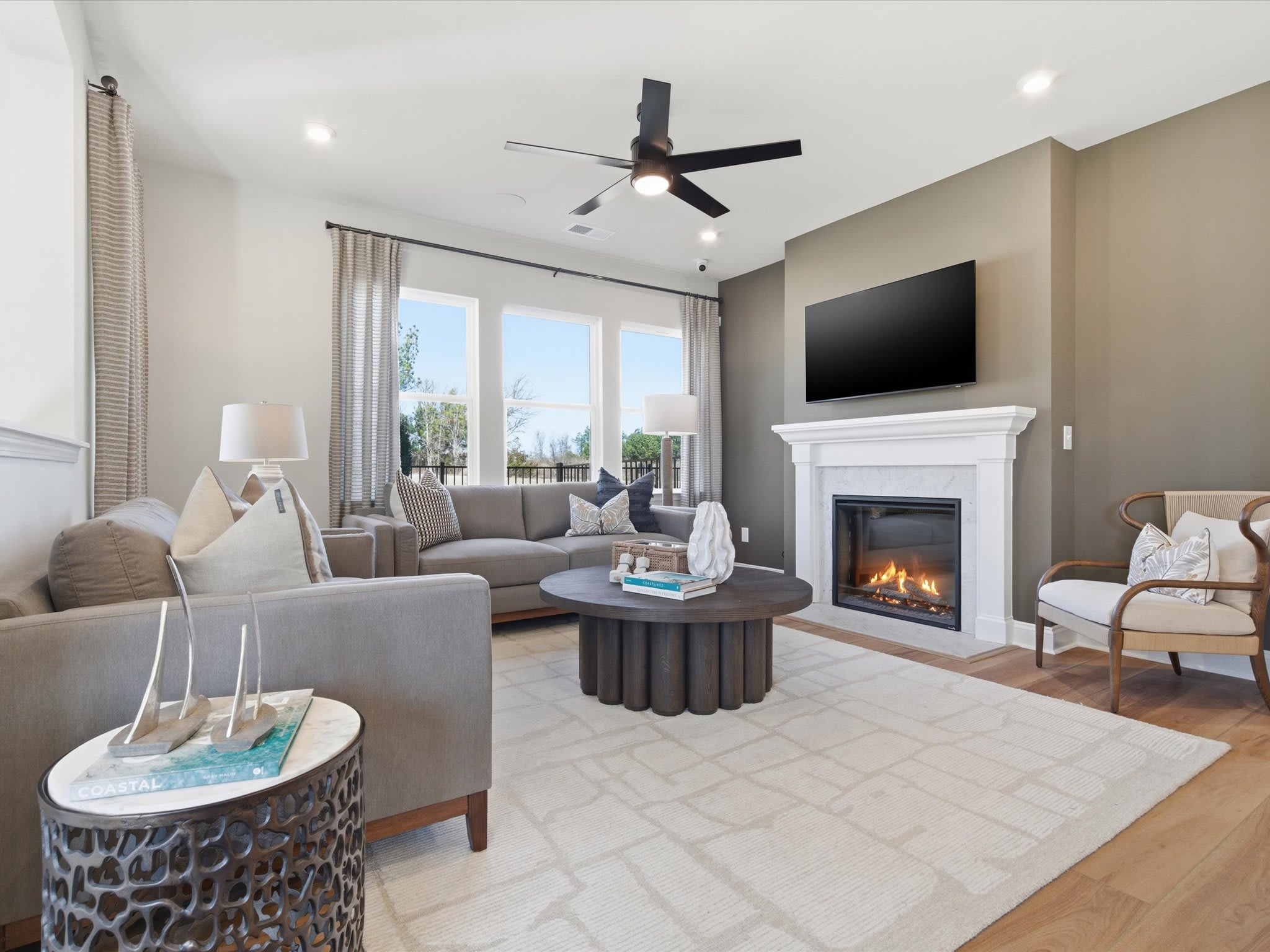 A cozy and inviting living room with a fireplace, comfortable seating, and a large television mounted on the wall, surrounded by natural light from the windows.