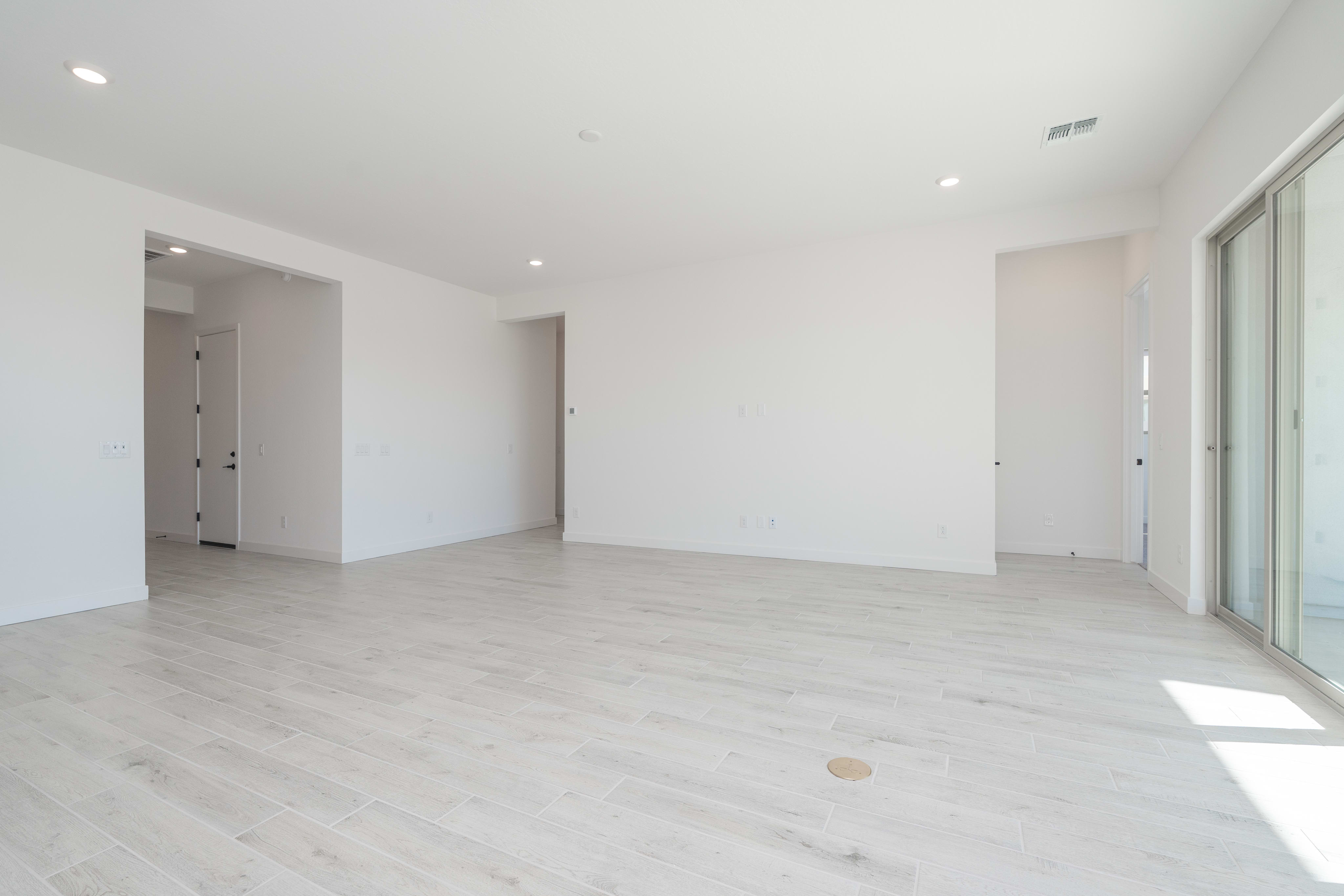 A spacious, bright room with white walls and light-colored hardwood flooring, featuring a sliding glass door leading to an outdoor area.