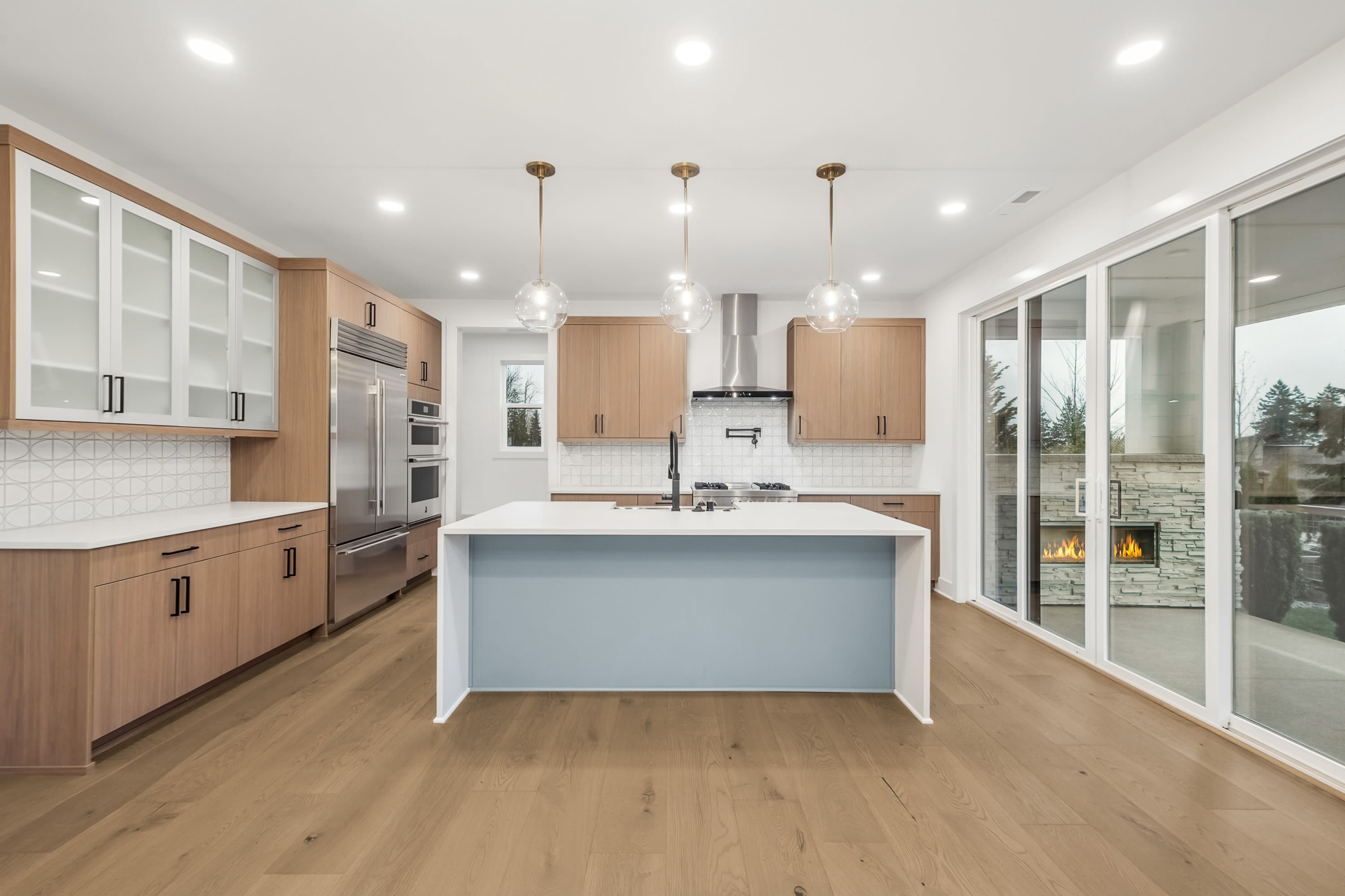 A modern, open-concept kitchen with light wood cabinets, a white island, and large windows overlooking a scenic outdoor view.