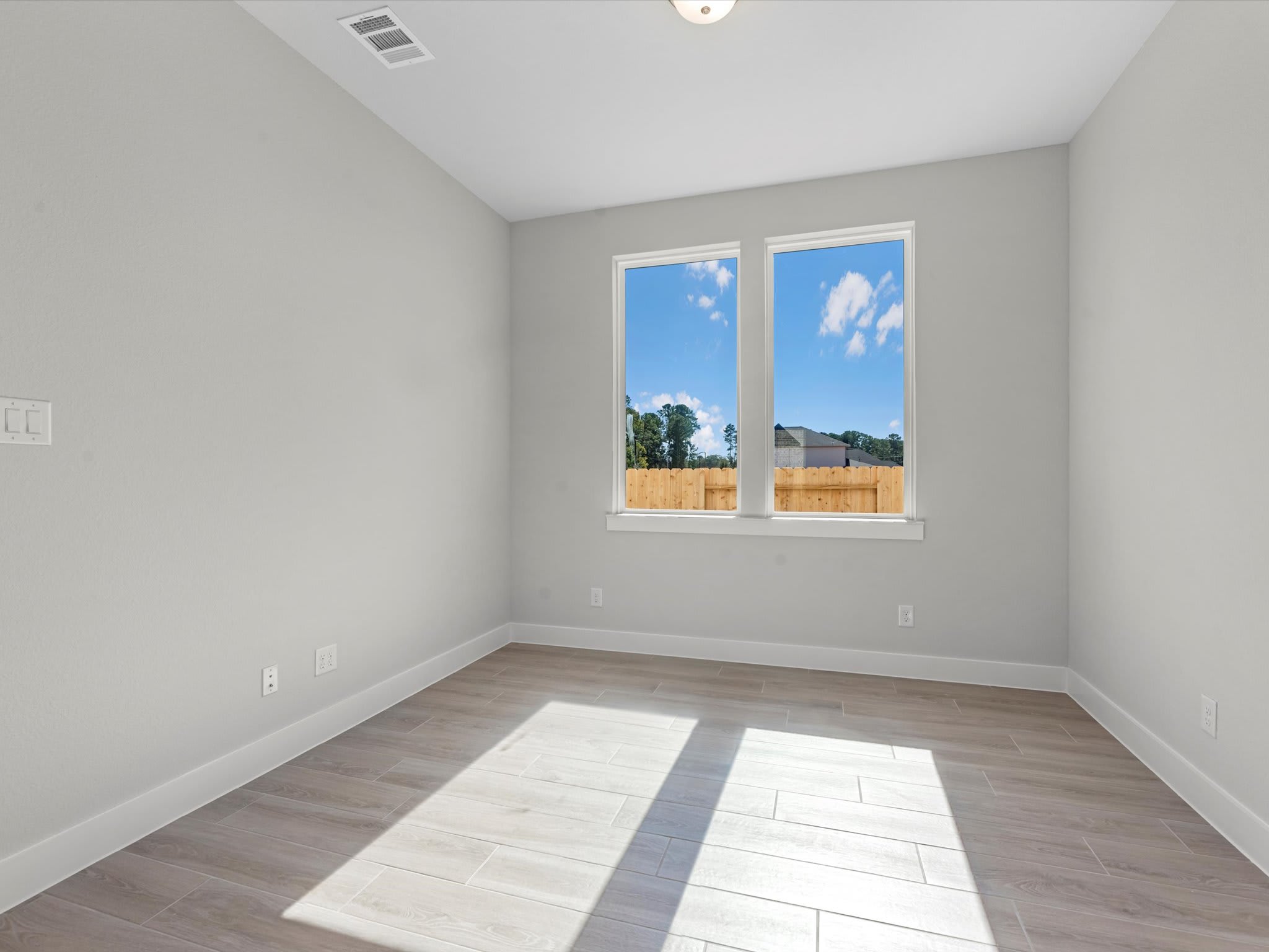An empty room with large windows overlooking a scenic outdoor landscape, featuring a hardwood floor and a neutral-colored wall.