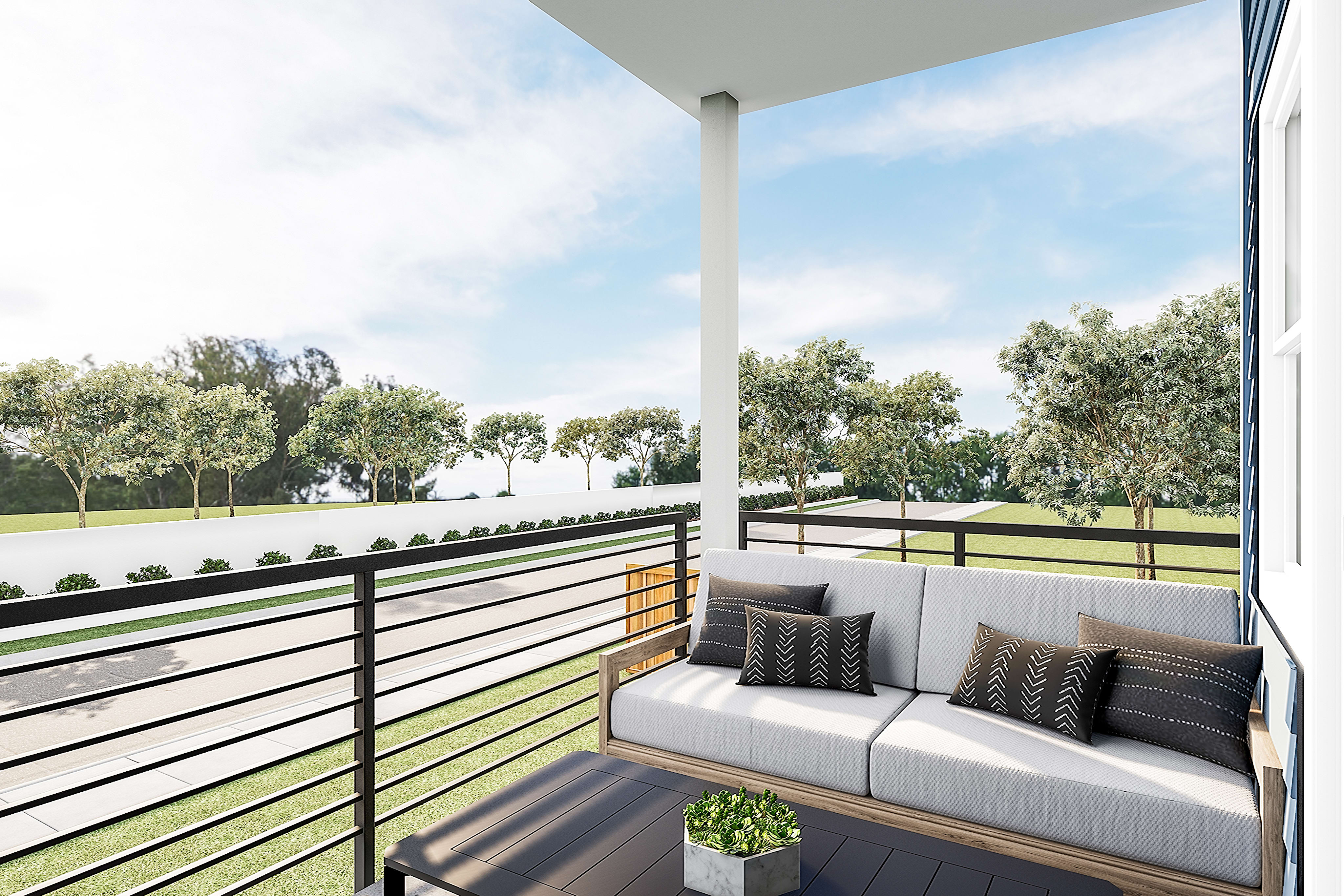 A balcony with a comfortable sofa and decorative pillows, overlooking a lush green landscape with trees and a clear sky.