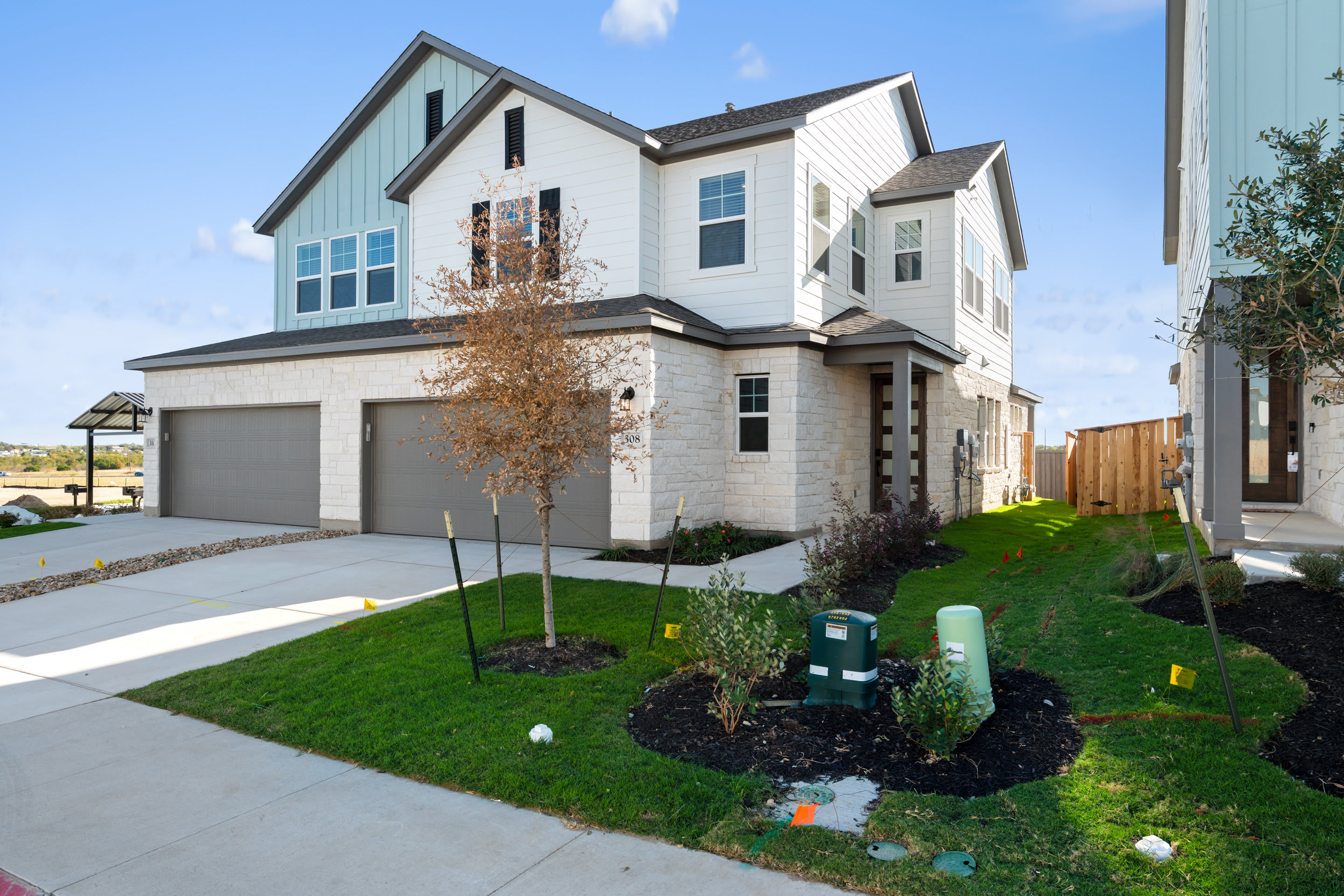 A modern two-story house with a well-maintained lawn and landscaping in the foreground, set against a clear blue sky in the background.