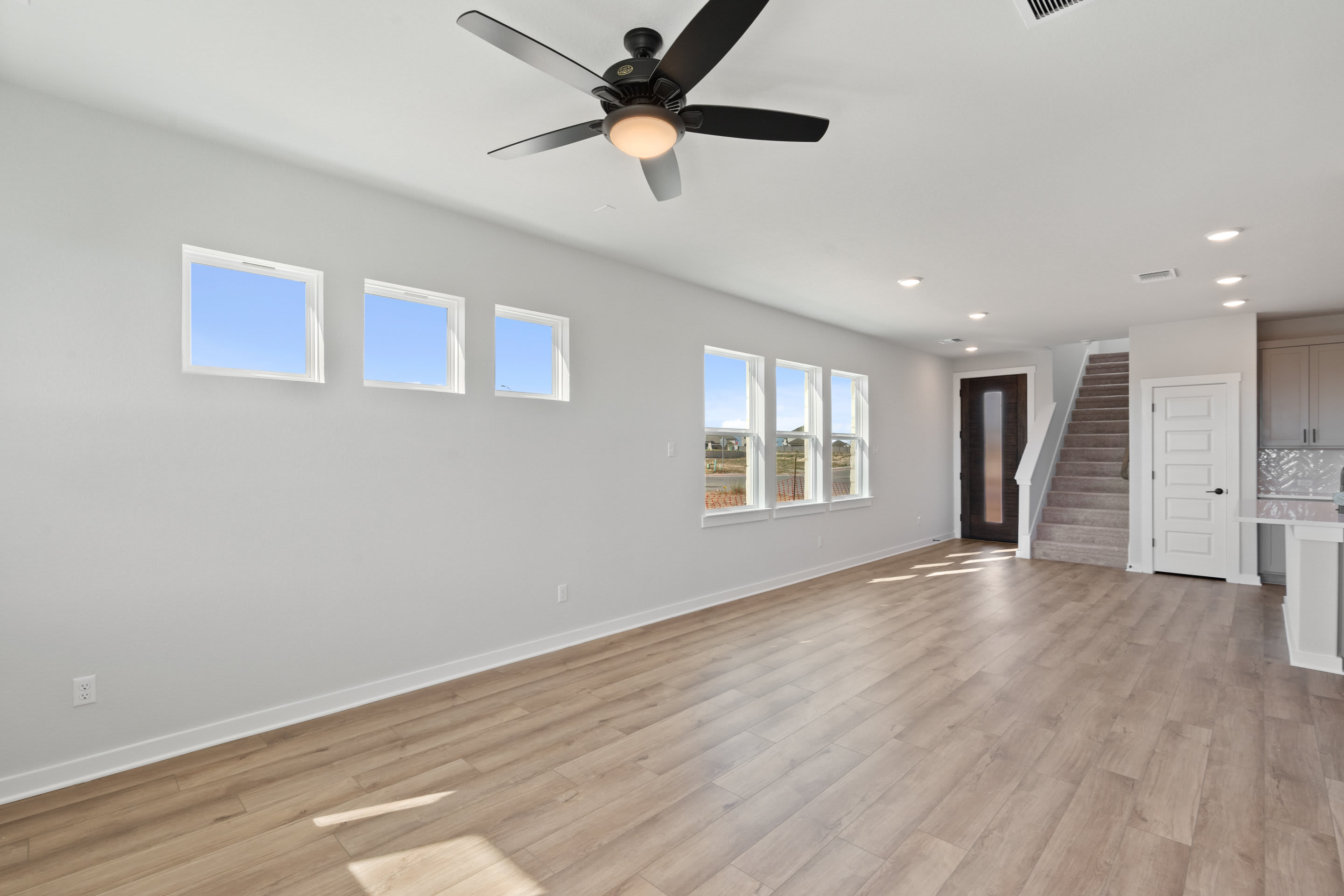 A spacious, well-lit room with a ceiling fan, hardwood floors, and large windows providing a view of the outdoors.