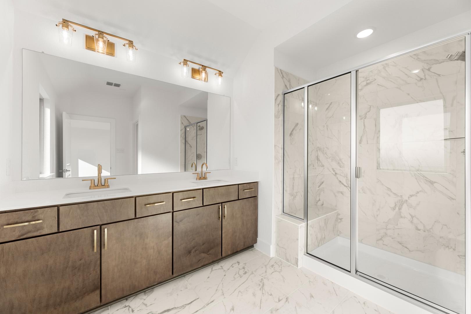 A modern and spacious bathroom with a large vanity, marble countertops, and a glass-enclosed shower area.