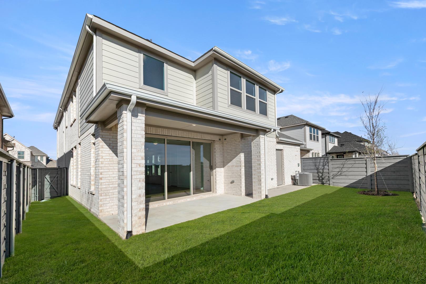 A modern two-story house with a well-manicured lawn in the foreground, set against a clear blue sky in the background.