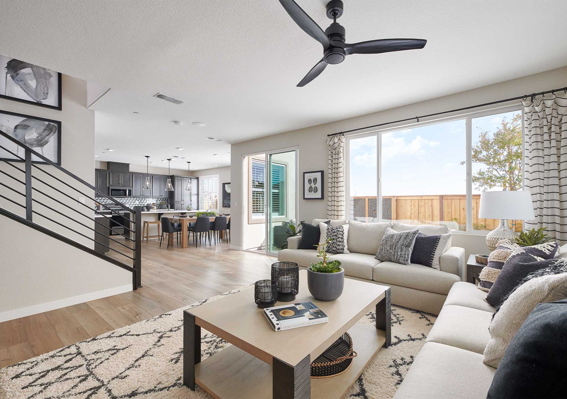 A modern and open-concept living space with a cozy seating area, a kitchen visible in the background, and a ceiling fan providing airflow.