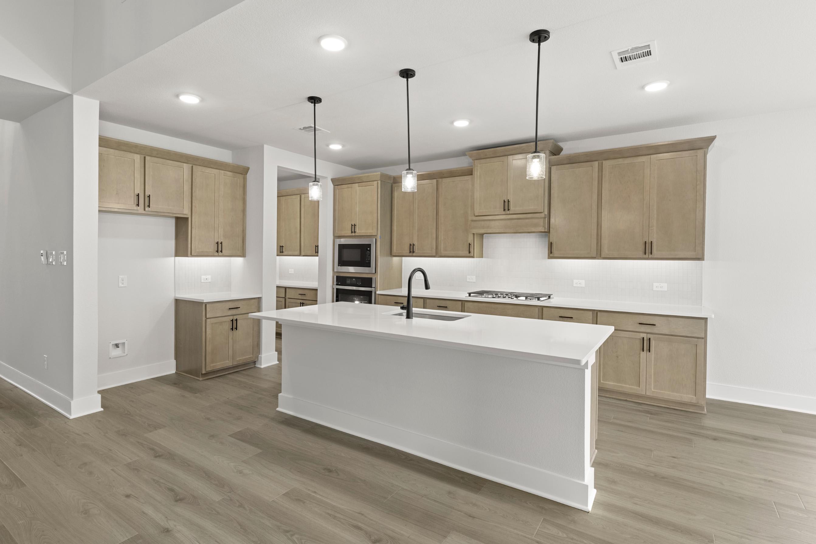 A modern, open-concept kitchen with light-colored wood cabinets, a white island, and pendant lighting fixtures.