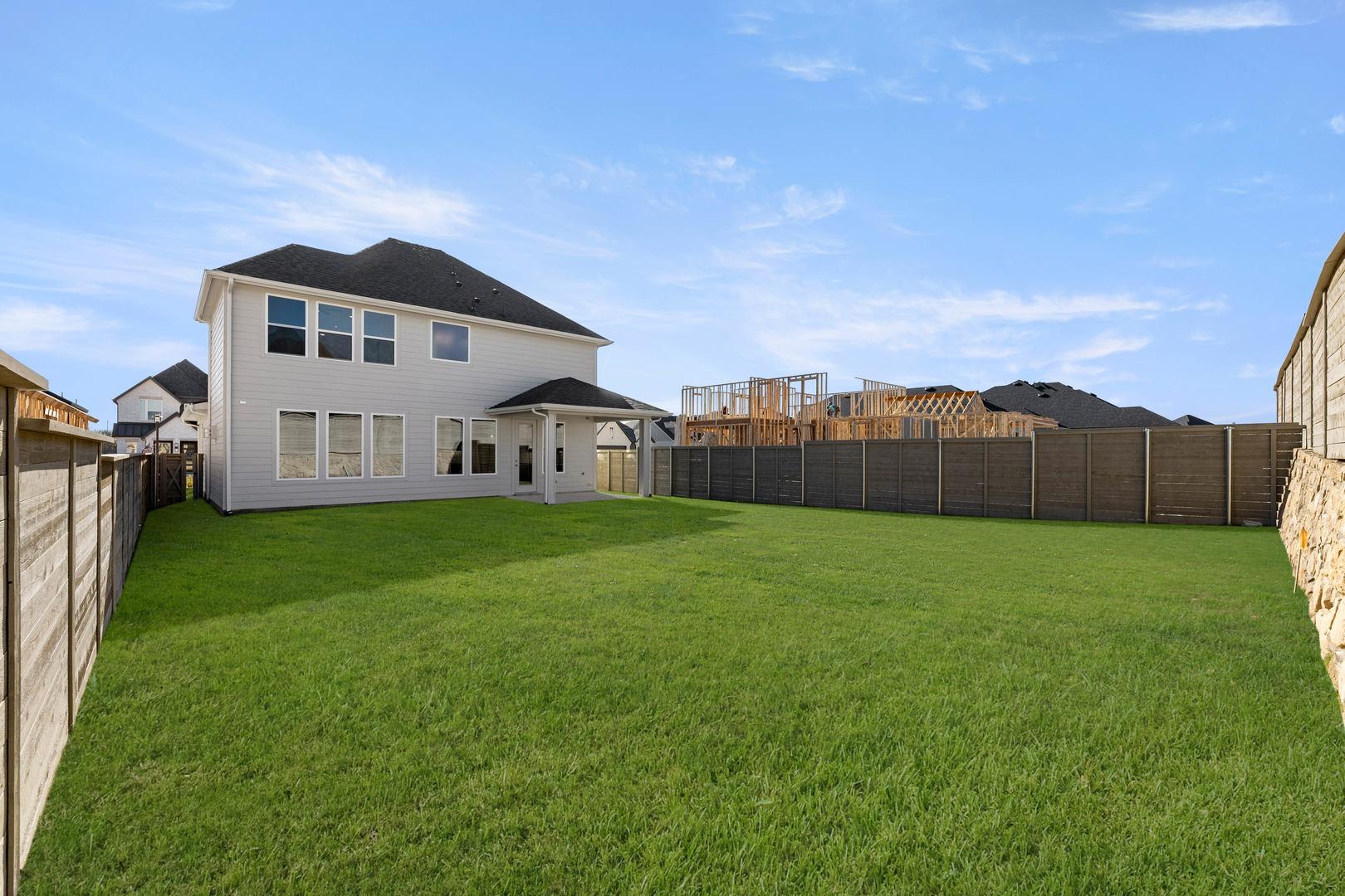 A large, two-story house with a well-manicured lawn and a wooden fence in the foreground, surrounded by a construction site in the background.