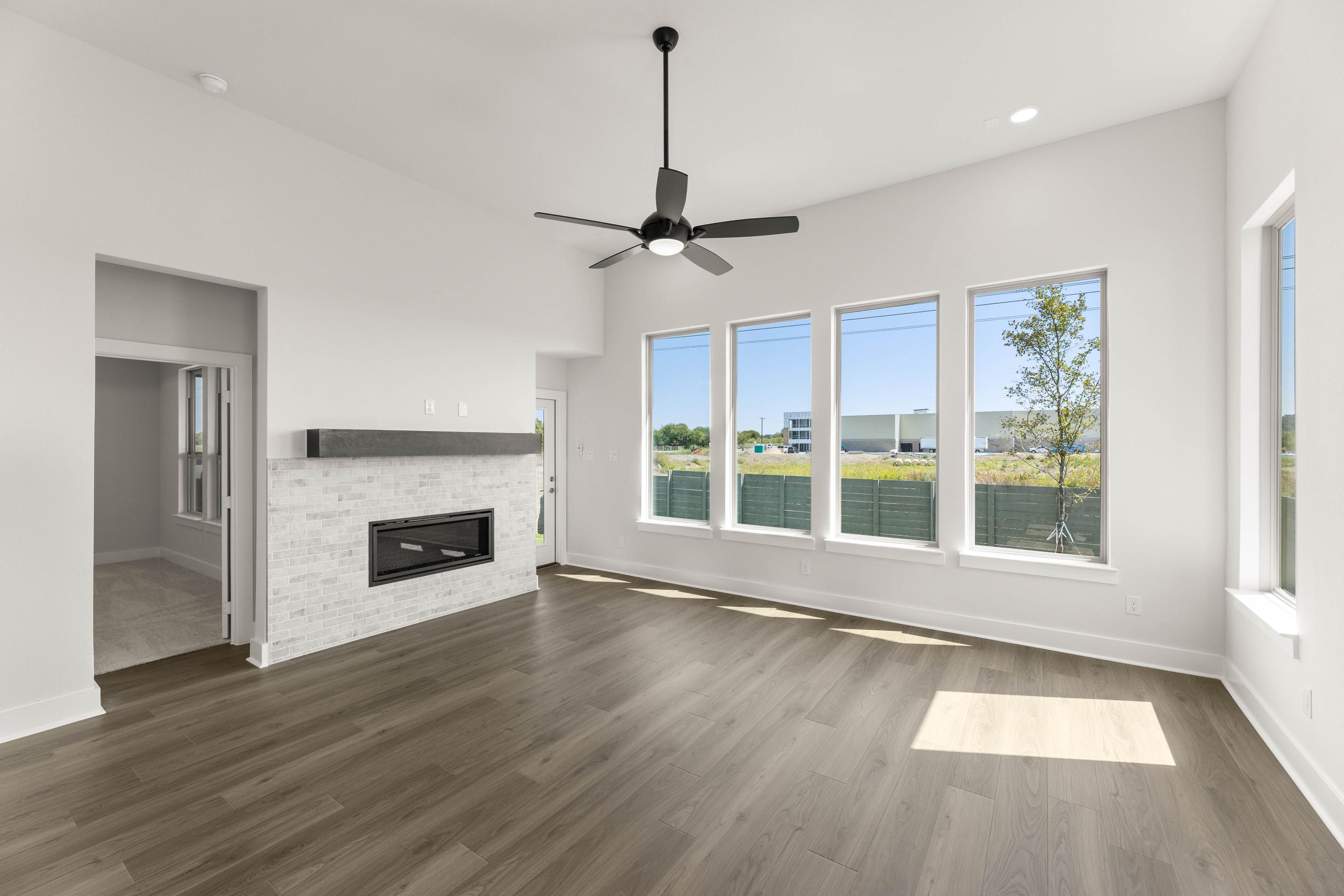 A spacious and bright room with a fireplace, hardwood floors, and large windows overlooking a scenic outdoor area.