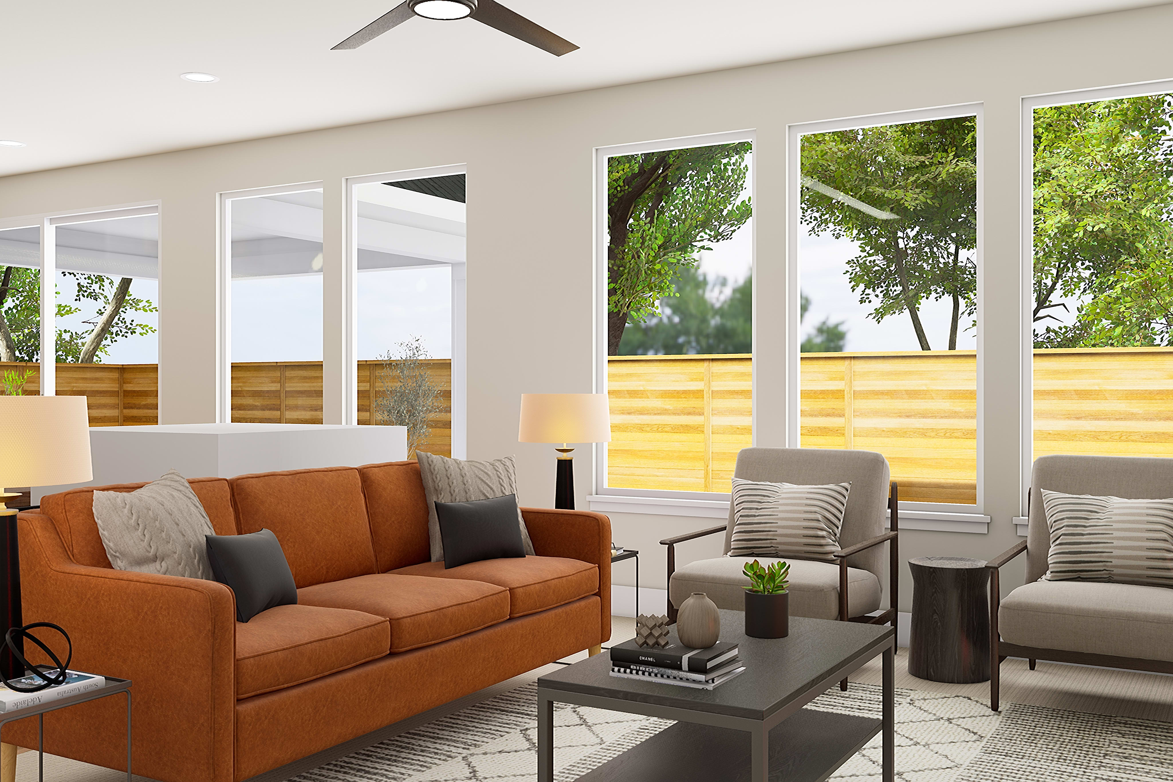 A cozy and modern living room with large windows overlooking a lush, green outdoor space, featuring an orange sofa, gray armchairs, and a sleek coffee table.