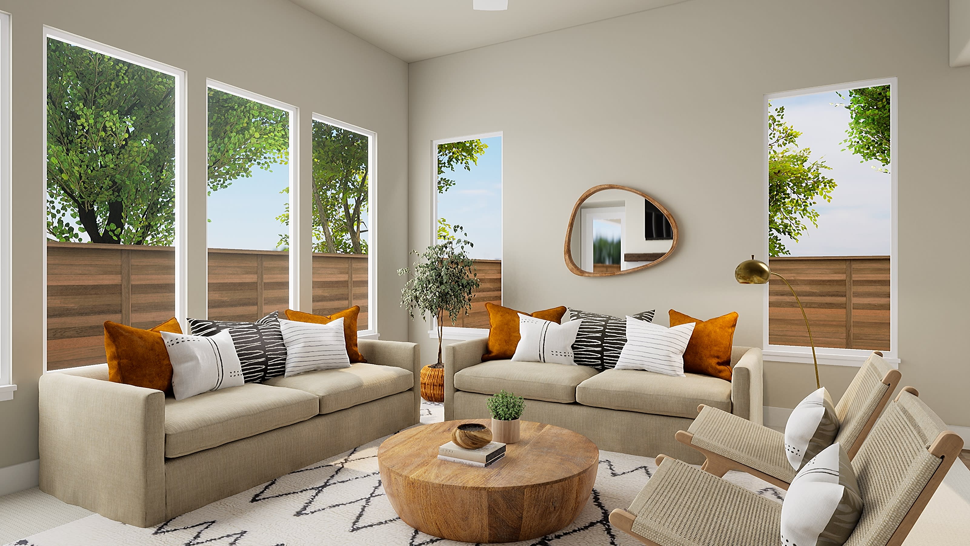 A cozy and inviting living room with large windows overlooking a lush, green outdoor space, featuring a pair of beige sofas adorned with patterned and solid throw pillows, a round wooden coffee table, and a decorative mirror on the wall.