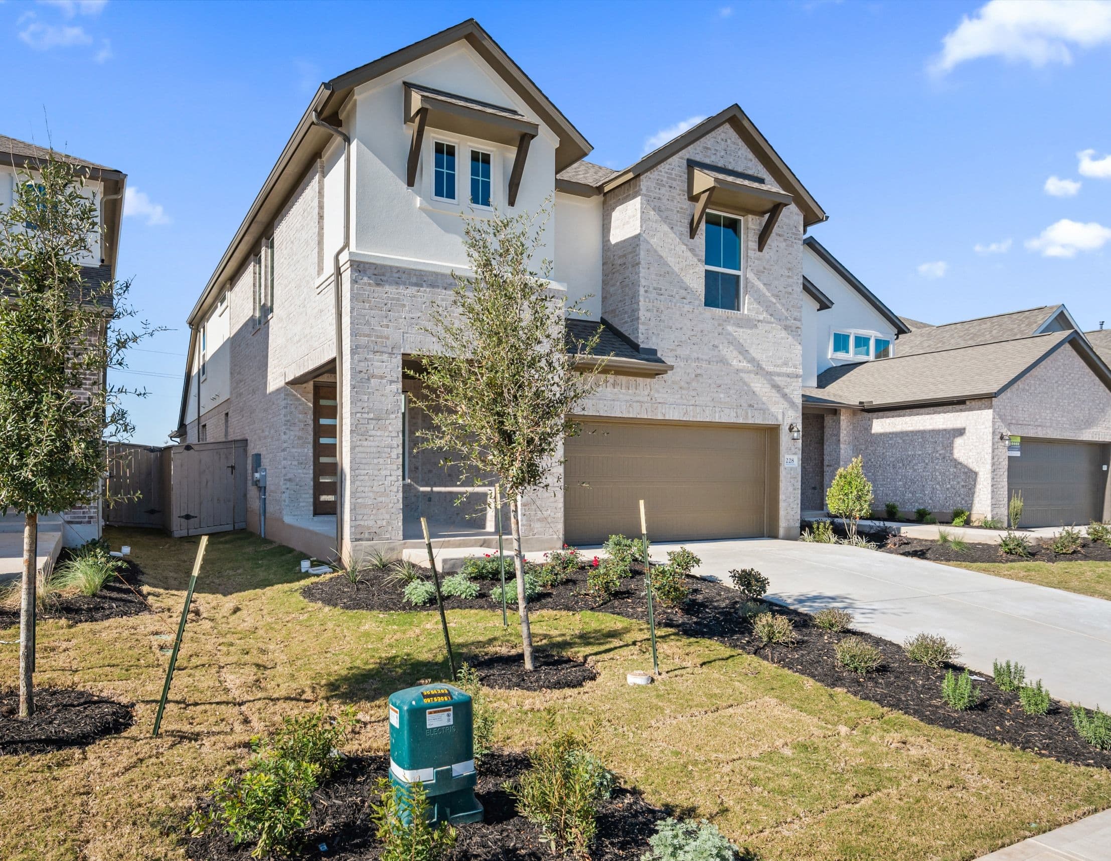 A newly constructed two-story residential building with a well-manicured lawn and landscaping in the foreground, set against a clear blue sky with some clouds.