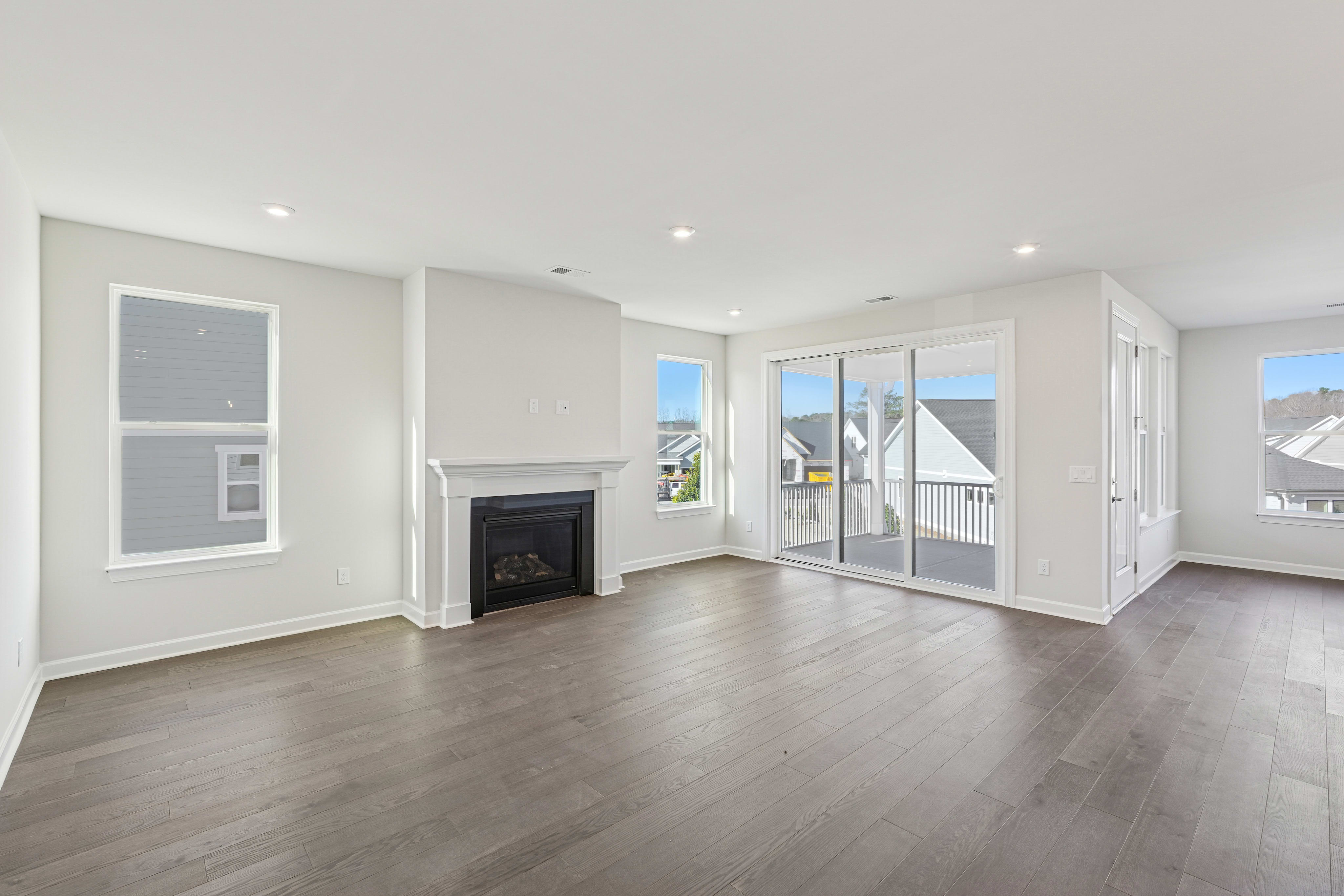 A spacious and bright living room with a fireplace, large windows, and hardwood floors. The room has a modern and minimalist design with a neutral color palette.