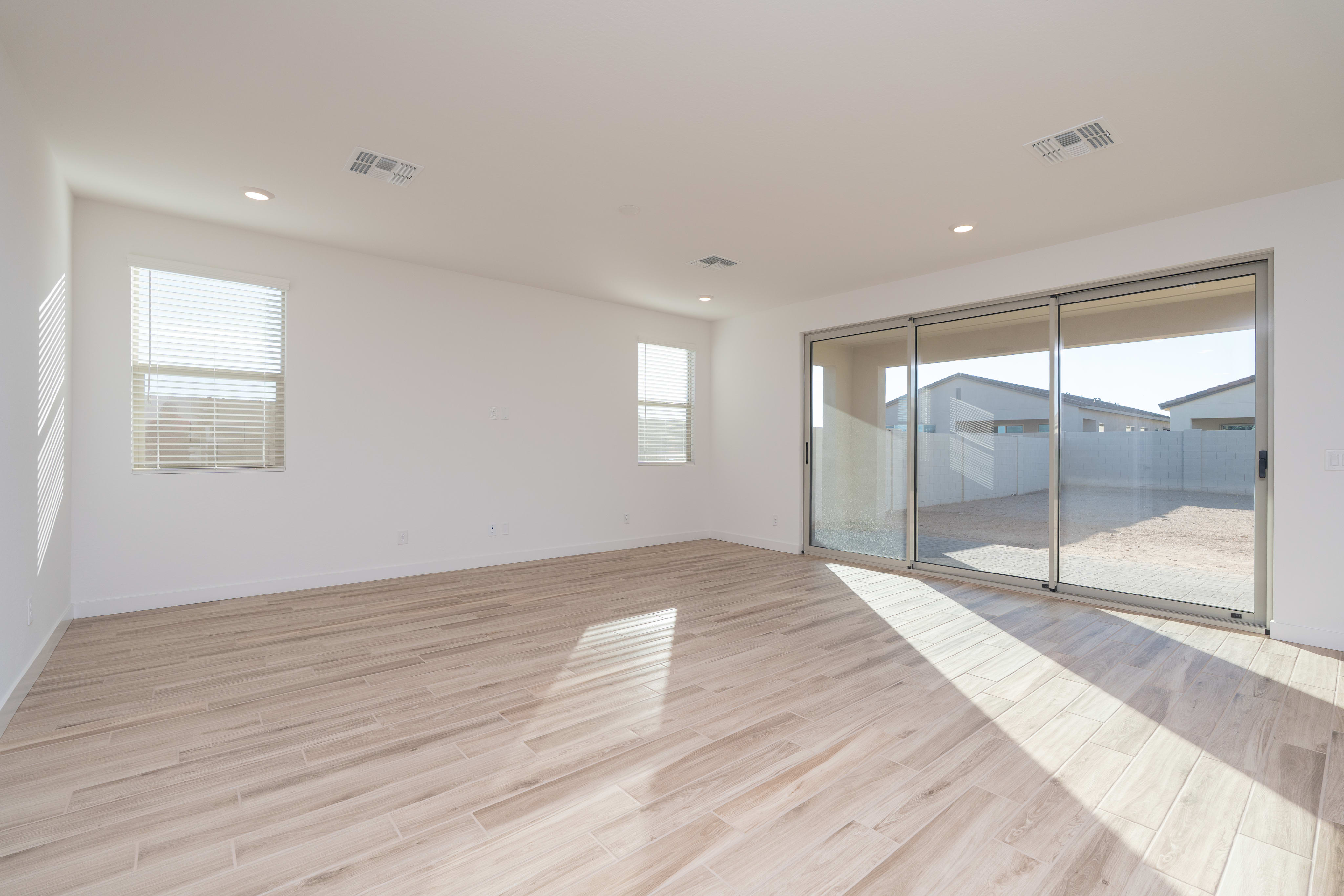 A spacious, well-lit room with a wooden floor, large windows, and a sliding glass door leading to an outdoor area.